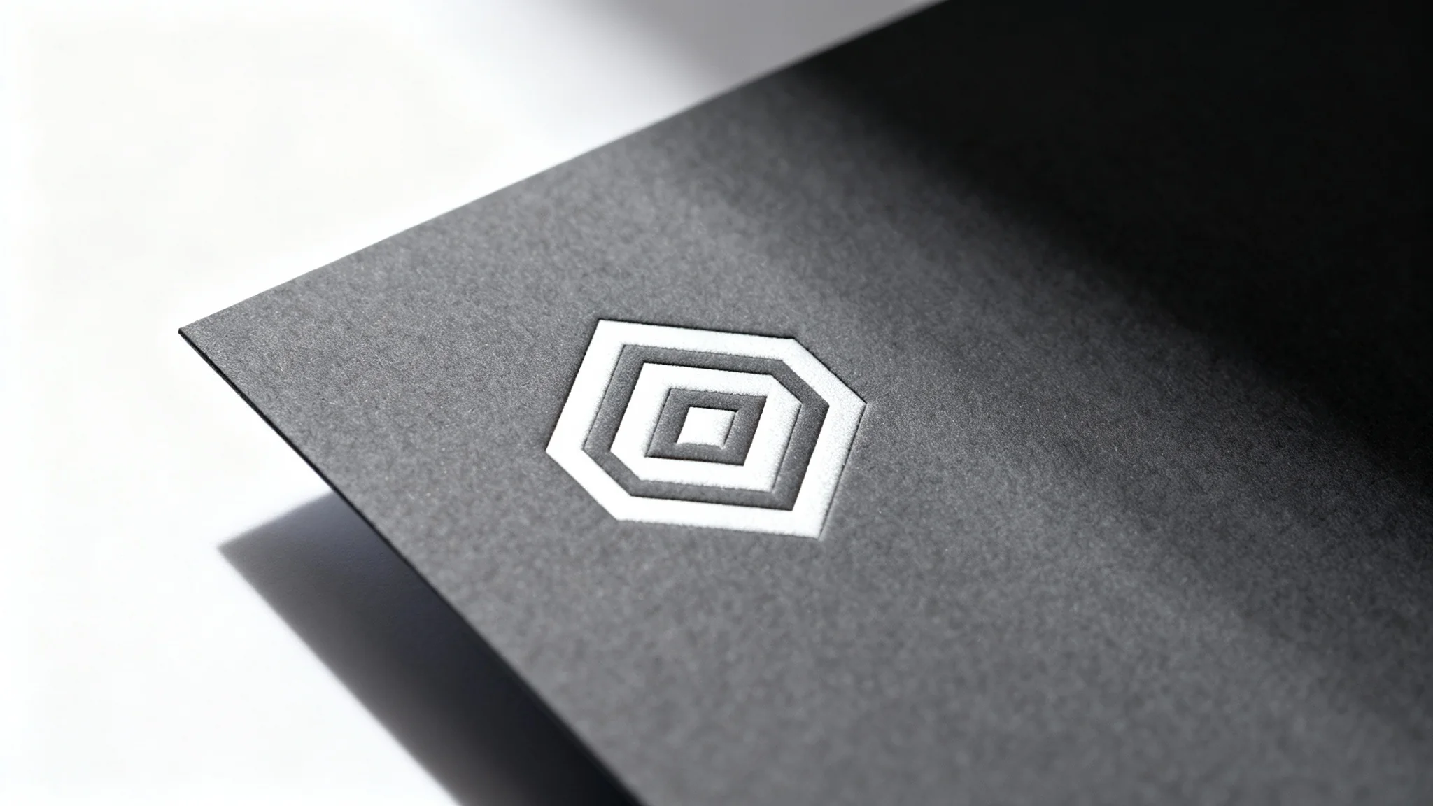 A photorealistic mockup of a minimalist white geometric logo, embossed on a dark gray textured card, isolated against a pure white background.