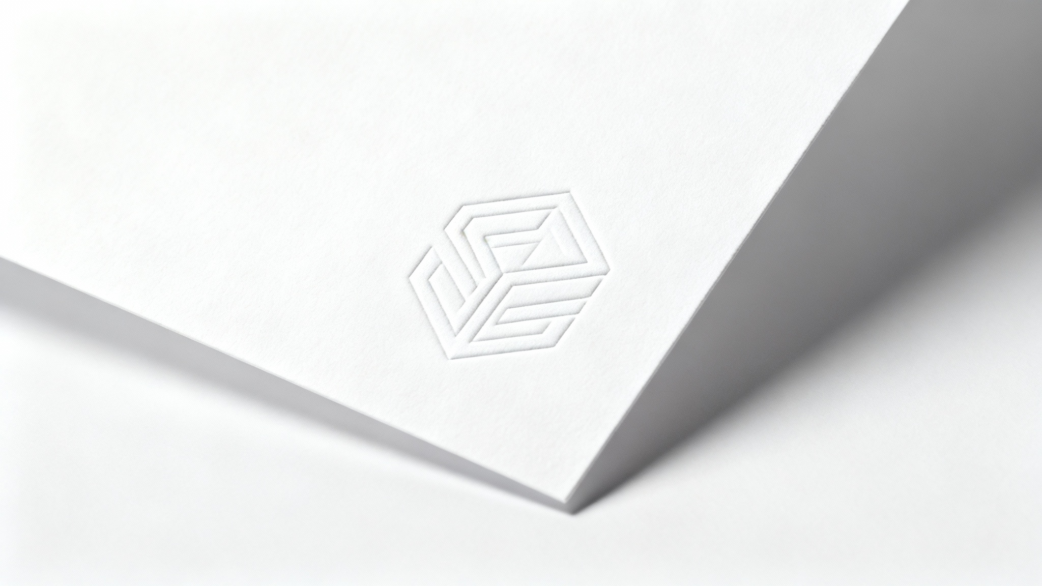 A minimalist white logo embossed onto a white paper background. The subtle shadows from the embossing create a sophisticated and clean white-on-white effect.