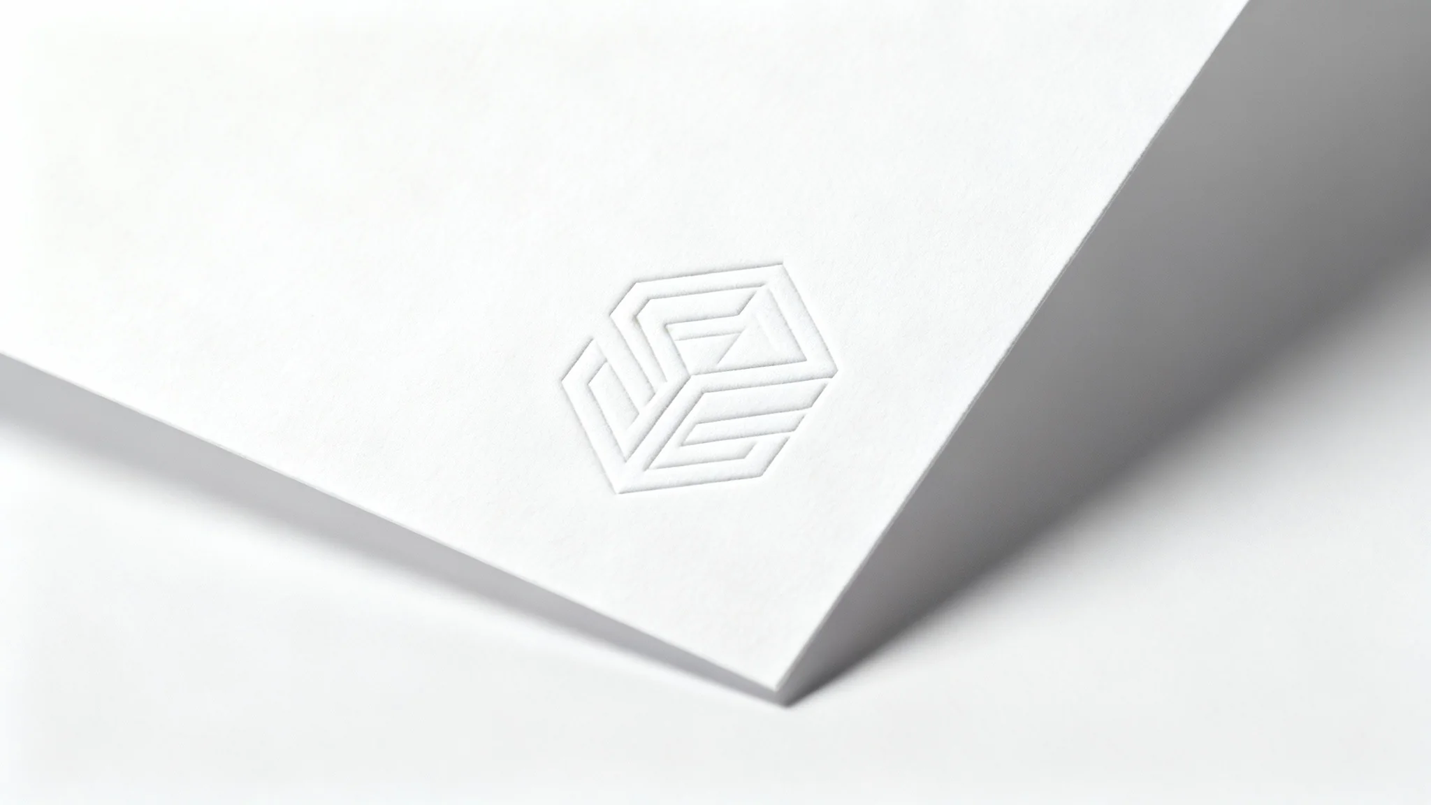 A minimalist white logo embossed onto a white paper background. The subtle shadows from the embossing create a sophisticated and clean white-on-white effect.