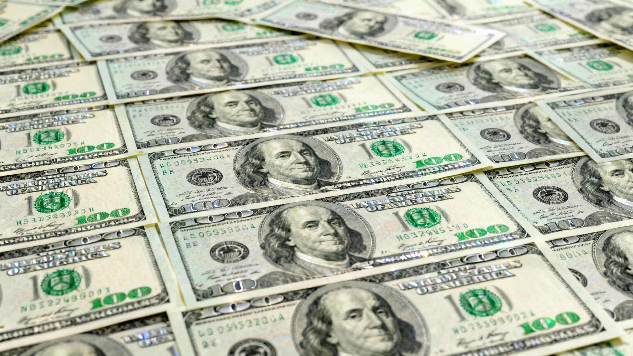 A top-down, detailed photograph of a textured surface made from a collage of overlapping one-hundred-dollar bills.