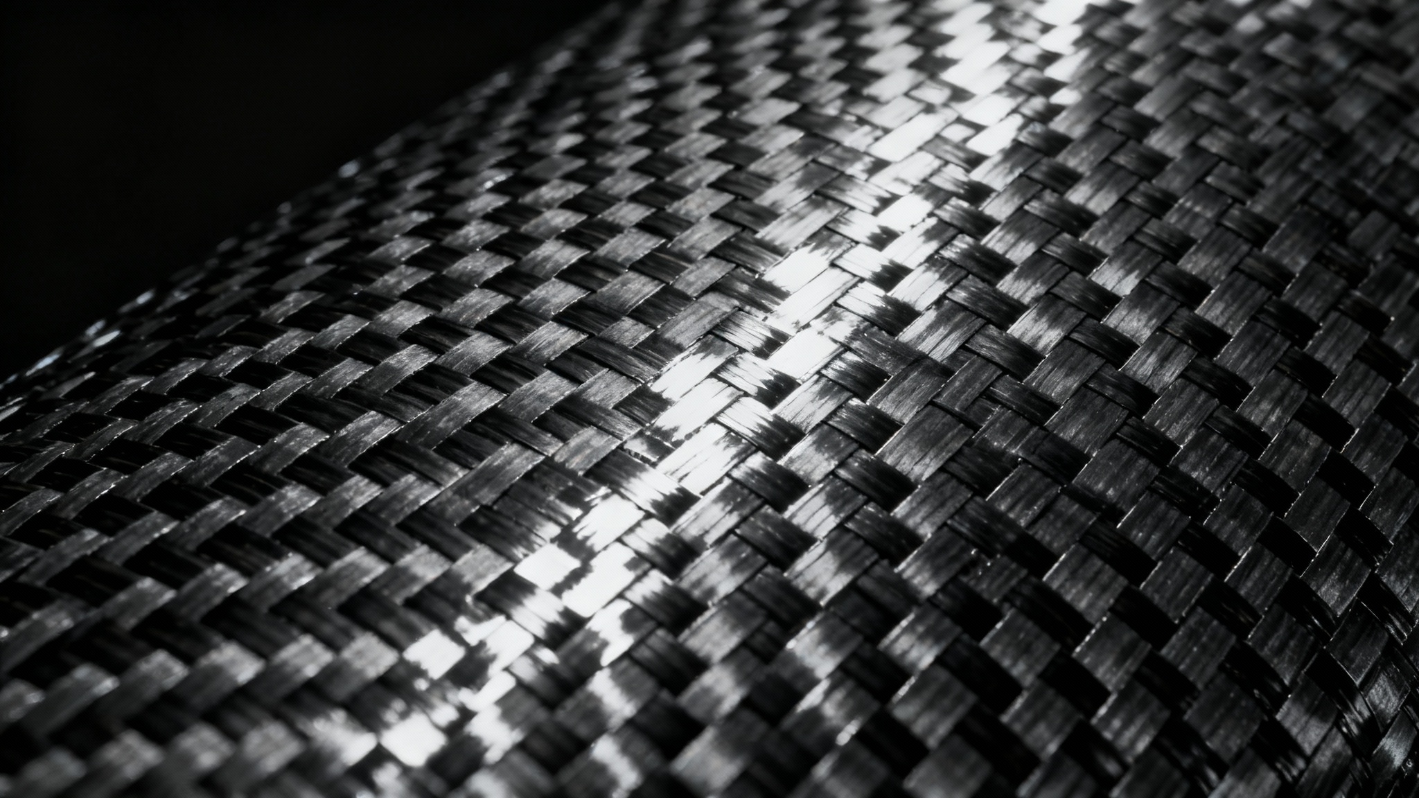 A close-up, detailed view of a black carbon fiber texture, showing its characteristic woven pattern and glossy finish under sharp lighting.