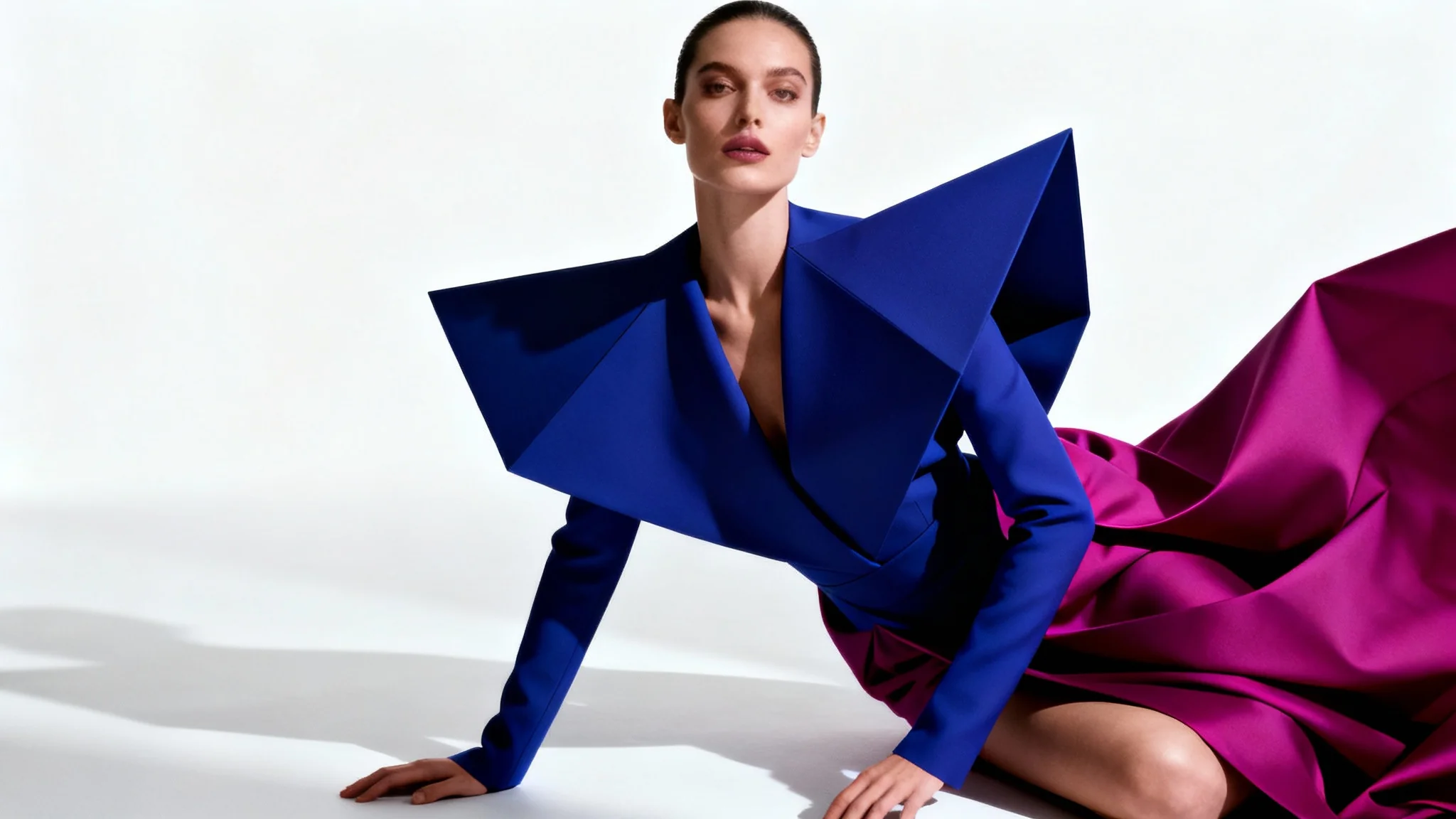 A fashion model in a striking, artistic outfit poses against a plain white background, captured in a dramatic, professional studio photograph.