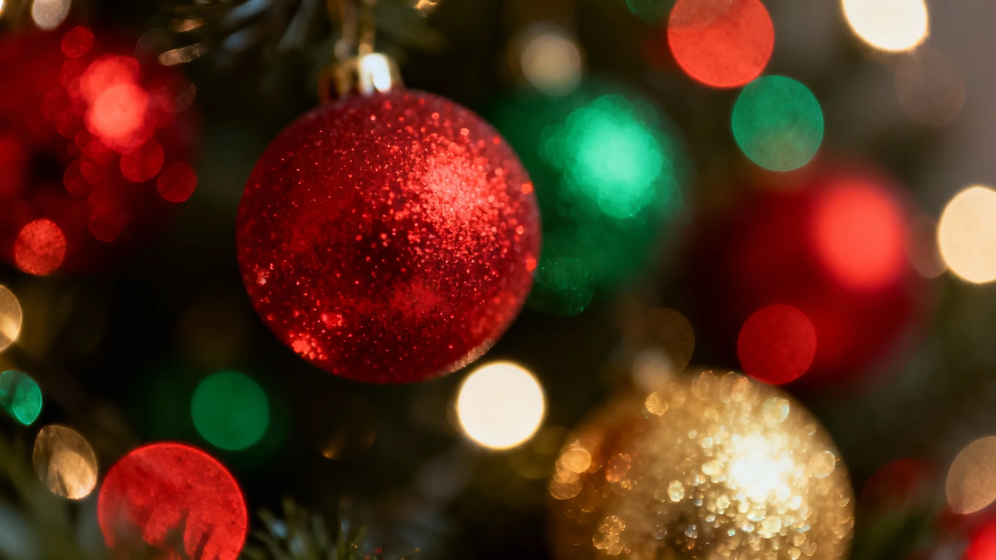 An abstract Christmas background featuring a dreamy bokeh effect. Shimmering, out-of-focus orbs of light in festive red, green, and gold glow against a dark backdrop, creating a warm and magical holiday atmosphere.