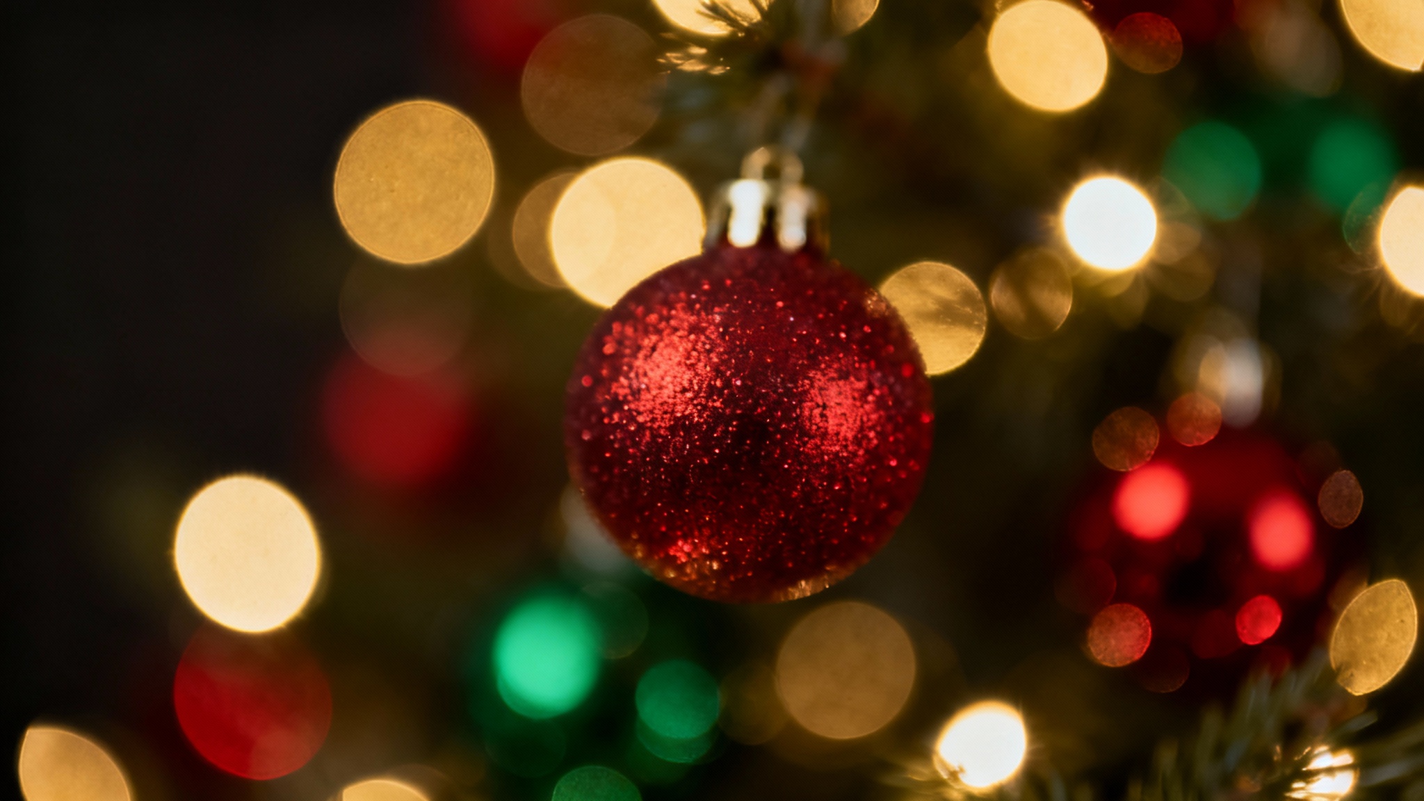 A festive Christmas background featuring a soft-focus bokeh effect with glowing red, green, and gold lights against a dark backdrop.