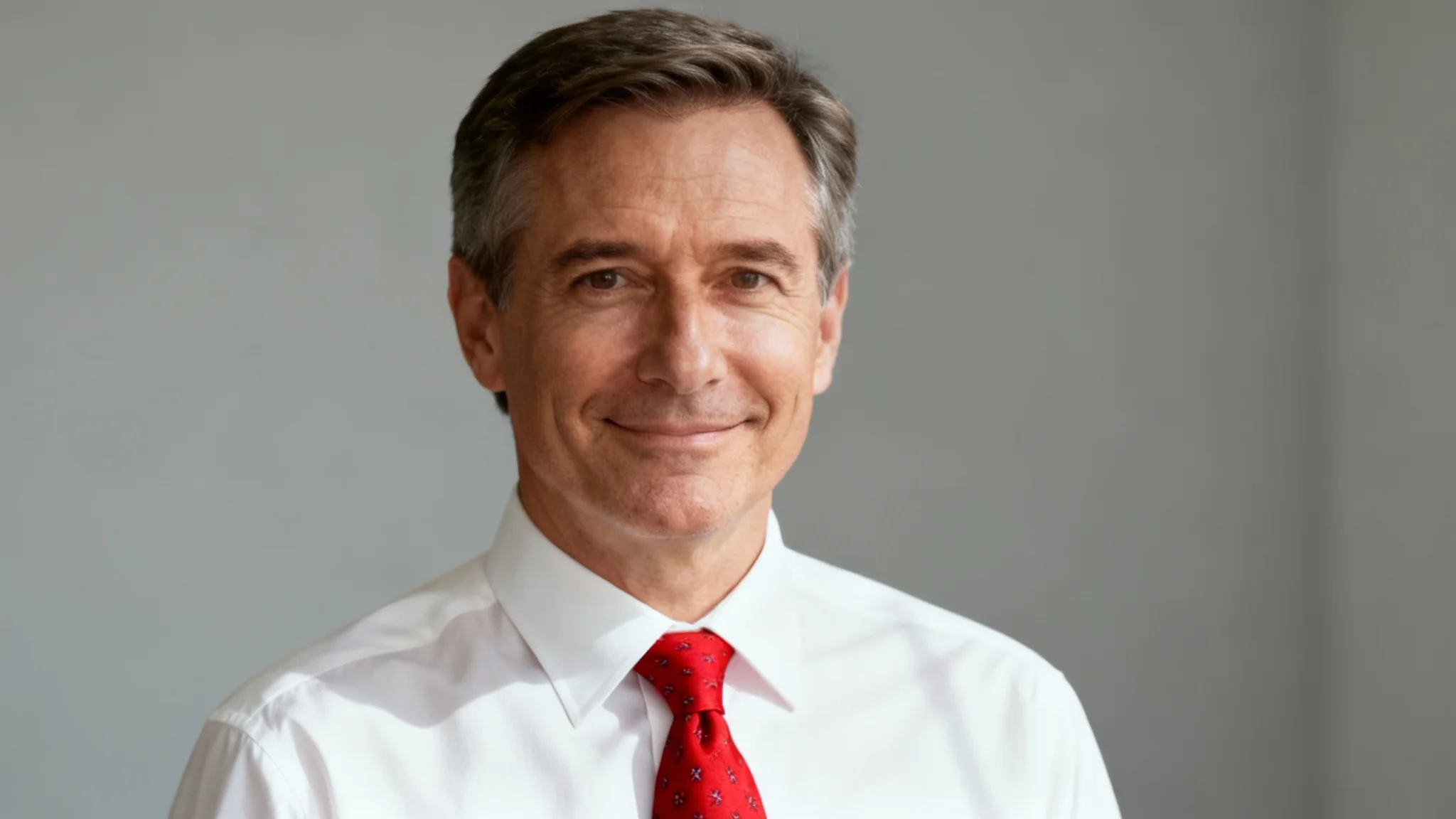 A professional headshot of a middle-aged man in a white dress shirt and a perfectly placed red patterned tie, smiling confidently against a gray background, representing the result of a photo-editing tool.