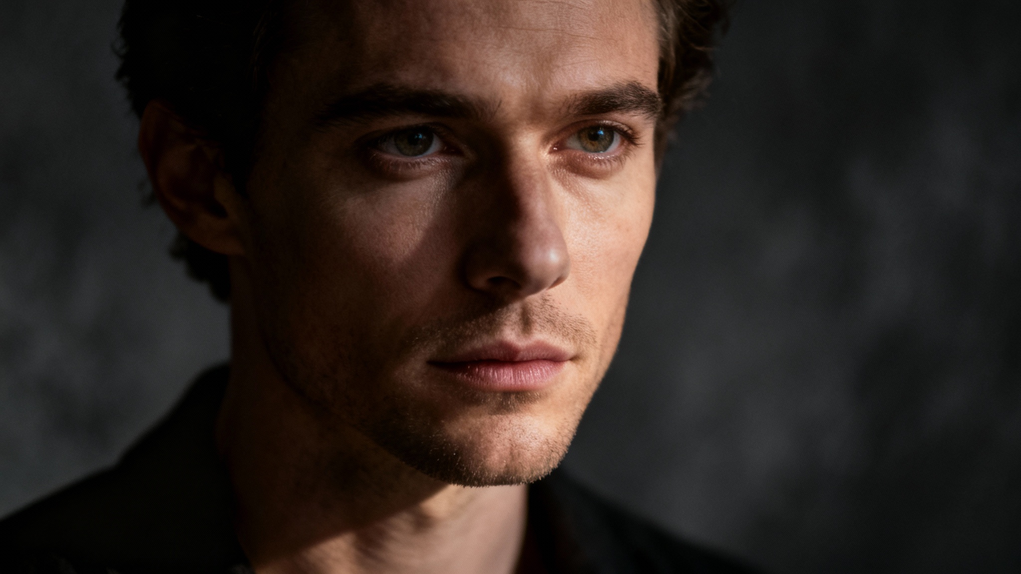 A professional studio portrait of a person with dramatic Rembrandt lighting, creating strong highlights and shadows across their face, set against a dark, out-of-focus studio background.