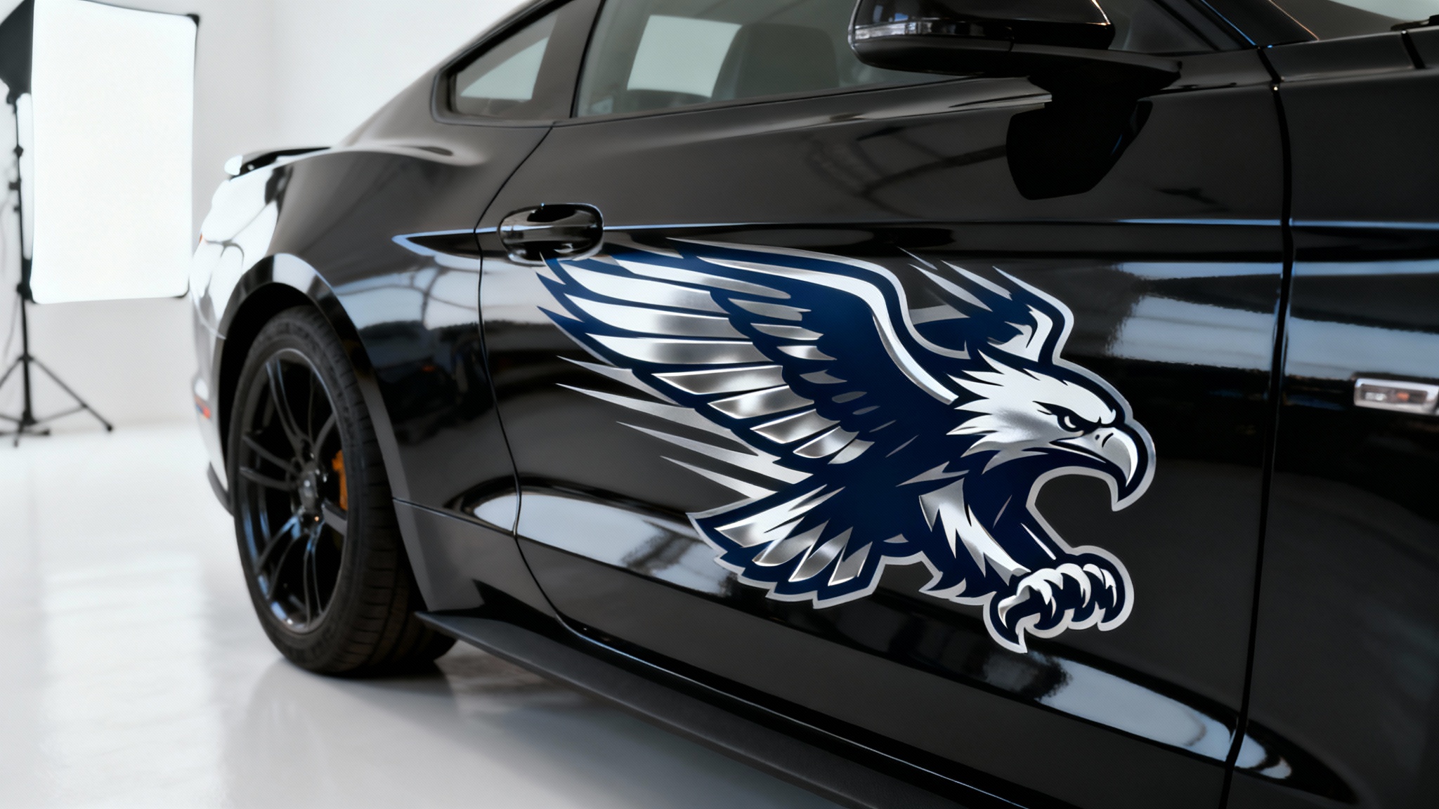 A close-up product shot of a metallic silver and navy blue eagle decal on the side of a polished black car, showcased against a clean white studio background.