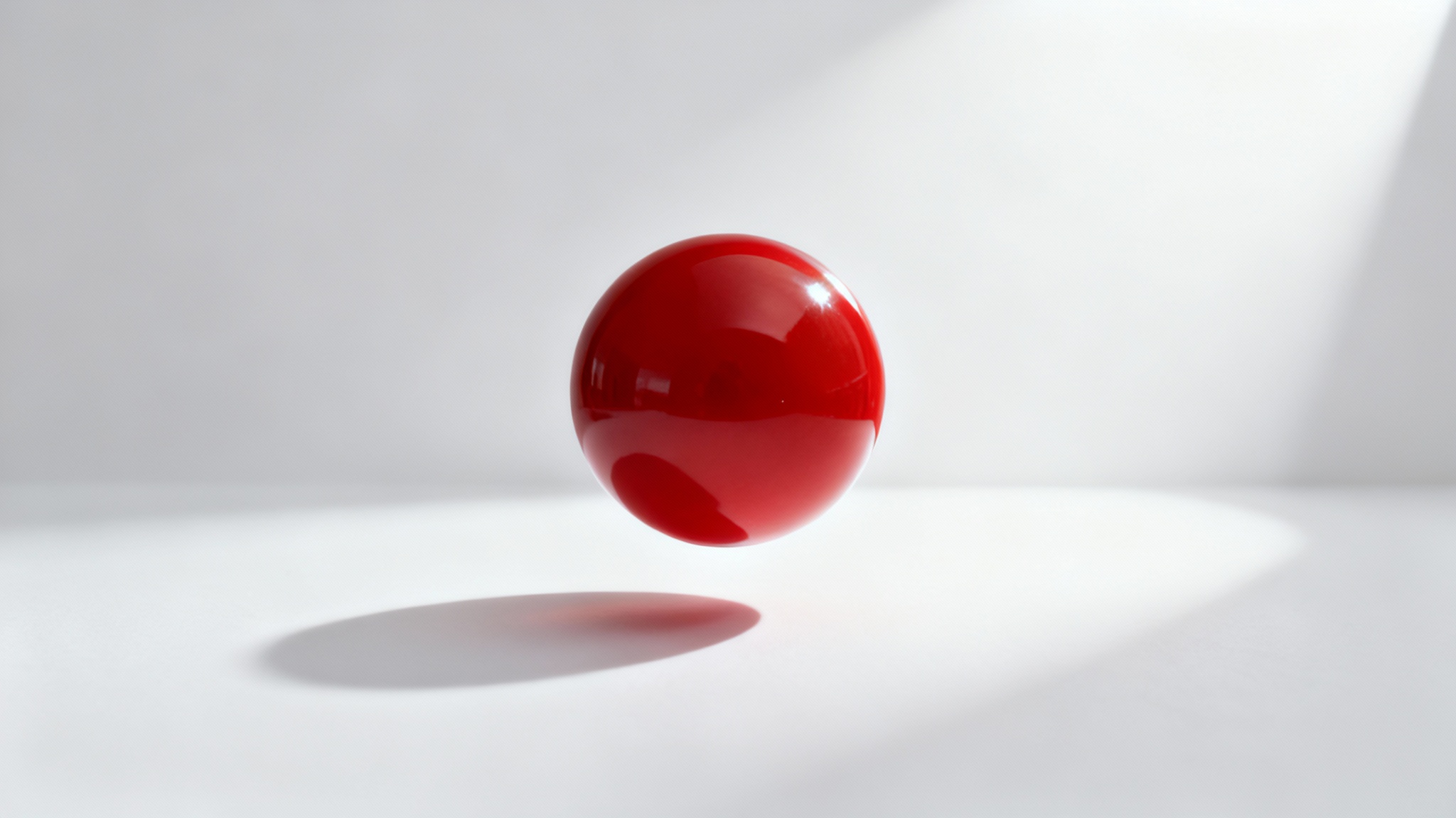 A photorealistic image of a red sphere floating above a white surface, casting a soft, realistic shadow.