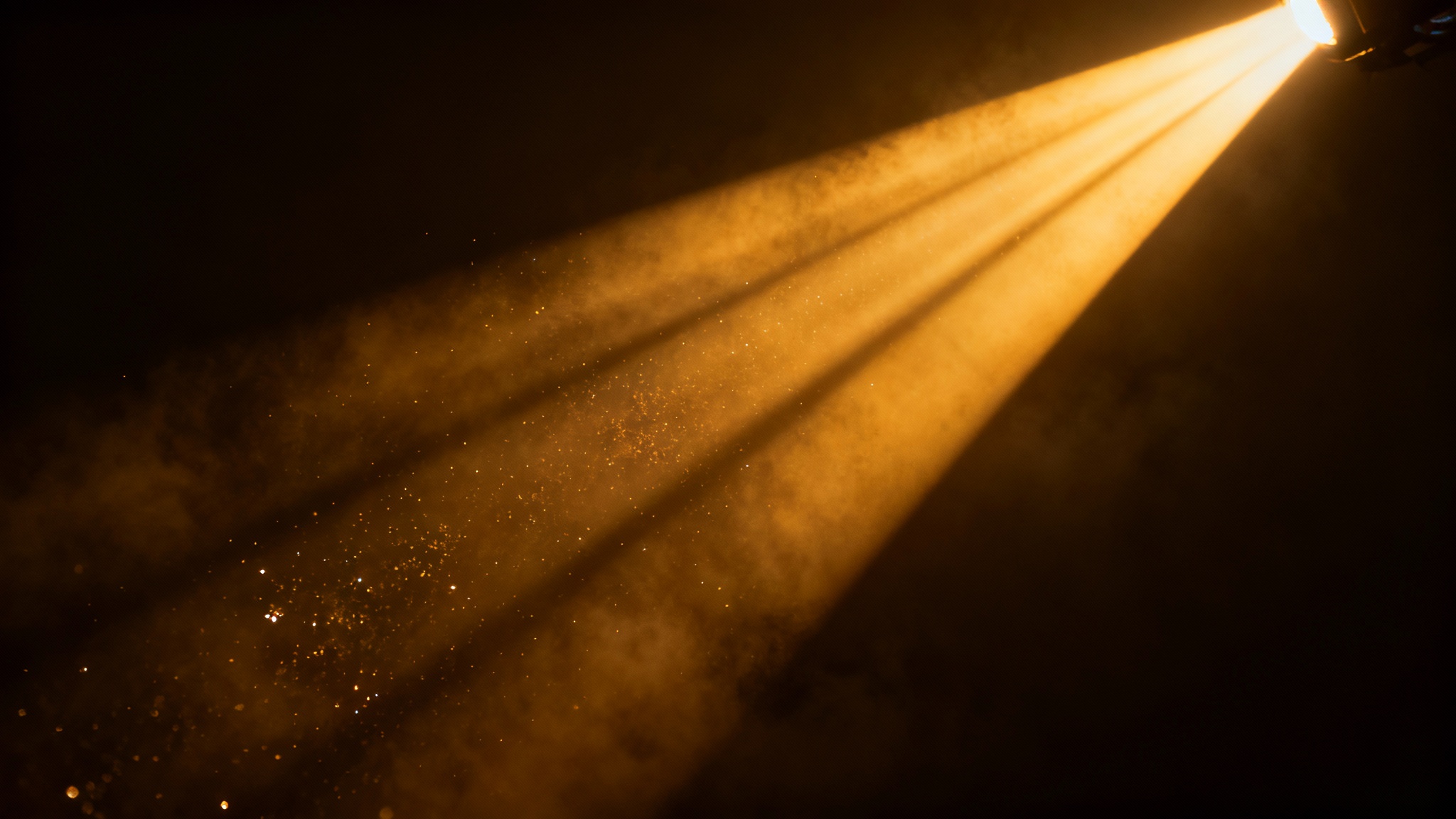 A dramatic, photorealistic image of cinematic light rays, with golden beams of light cutting through a dark, hazy atmosphere against a clean background.