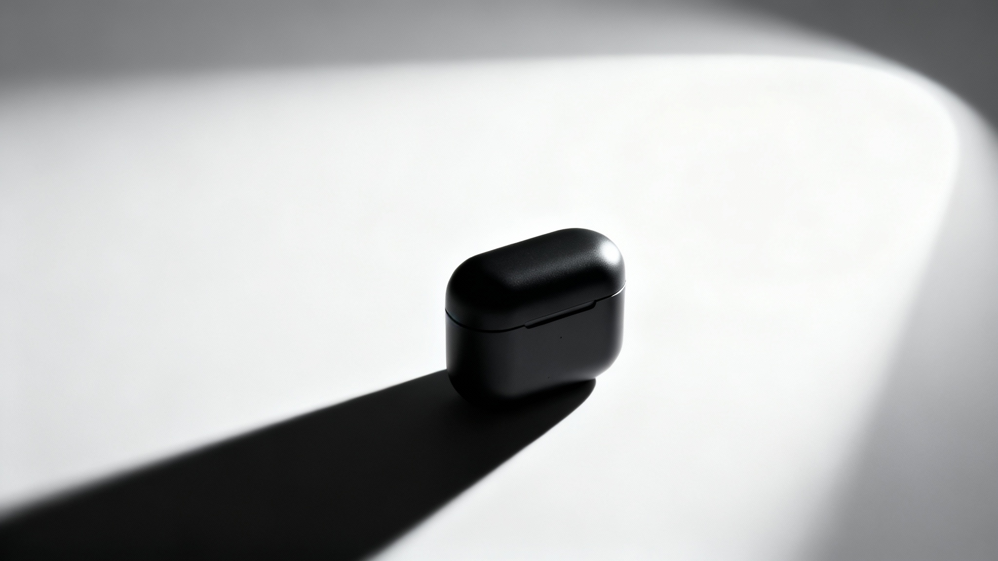A photorealistic image of a sleek, matte black product on a white background, dramatically lit by a single spotlight from the side, casting a long, sharp shadow. This image exemplifies dramatic product lighting.