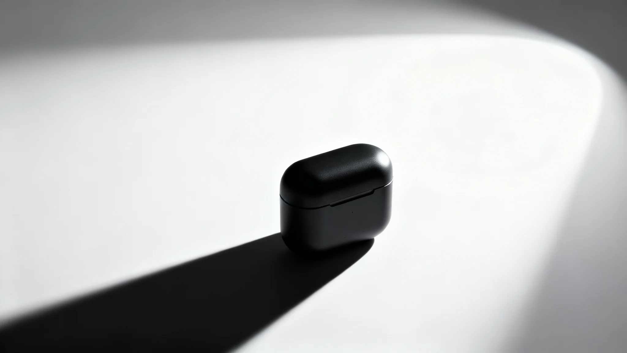 A photorealistic image of a sleek, matte black product on a white background, dramatically lit by a single spotlight from the side, casting a long, sharp shadow. This image exemplifies dramatic product lighting.