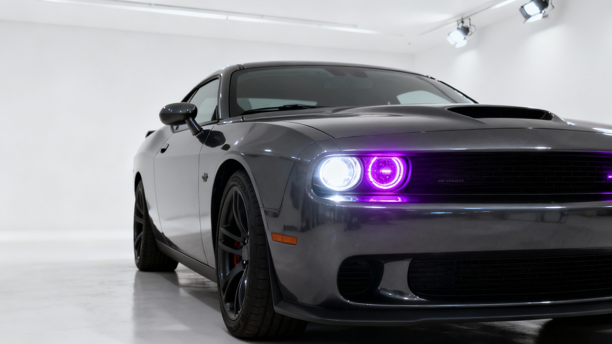 A close-up, dramatic shot of a dark grey sports car on a white background, with one headlight glowing white and the other glowing a vibrant purple to show a color change effect.
