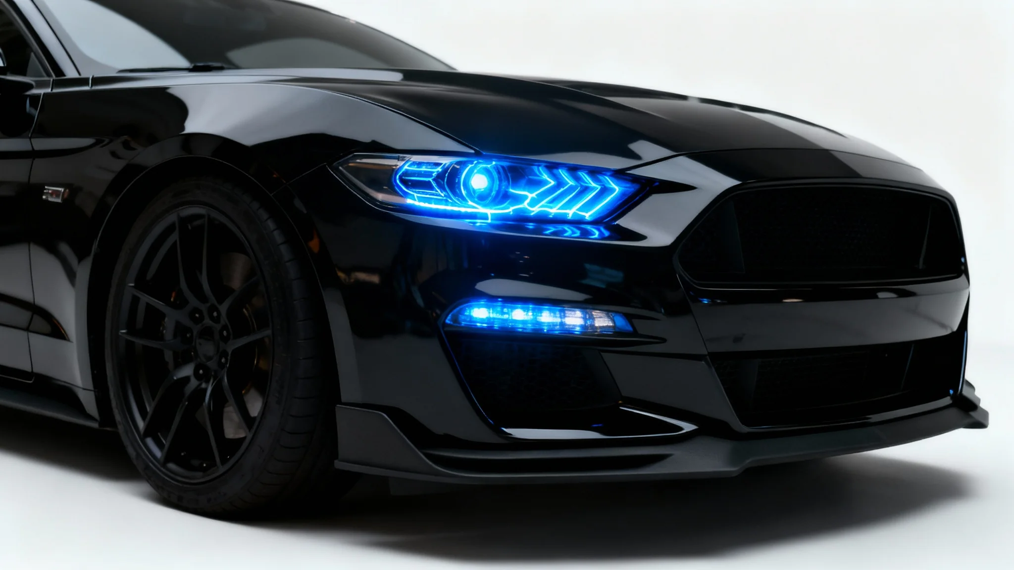 A close-up of a modern black sports car's headlight, which is glowing with a bright electric blue color, set against a clean white background.