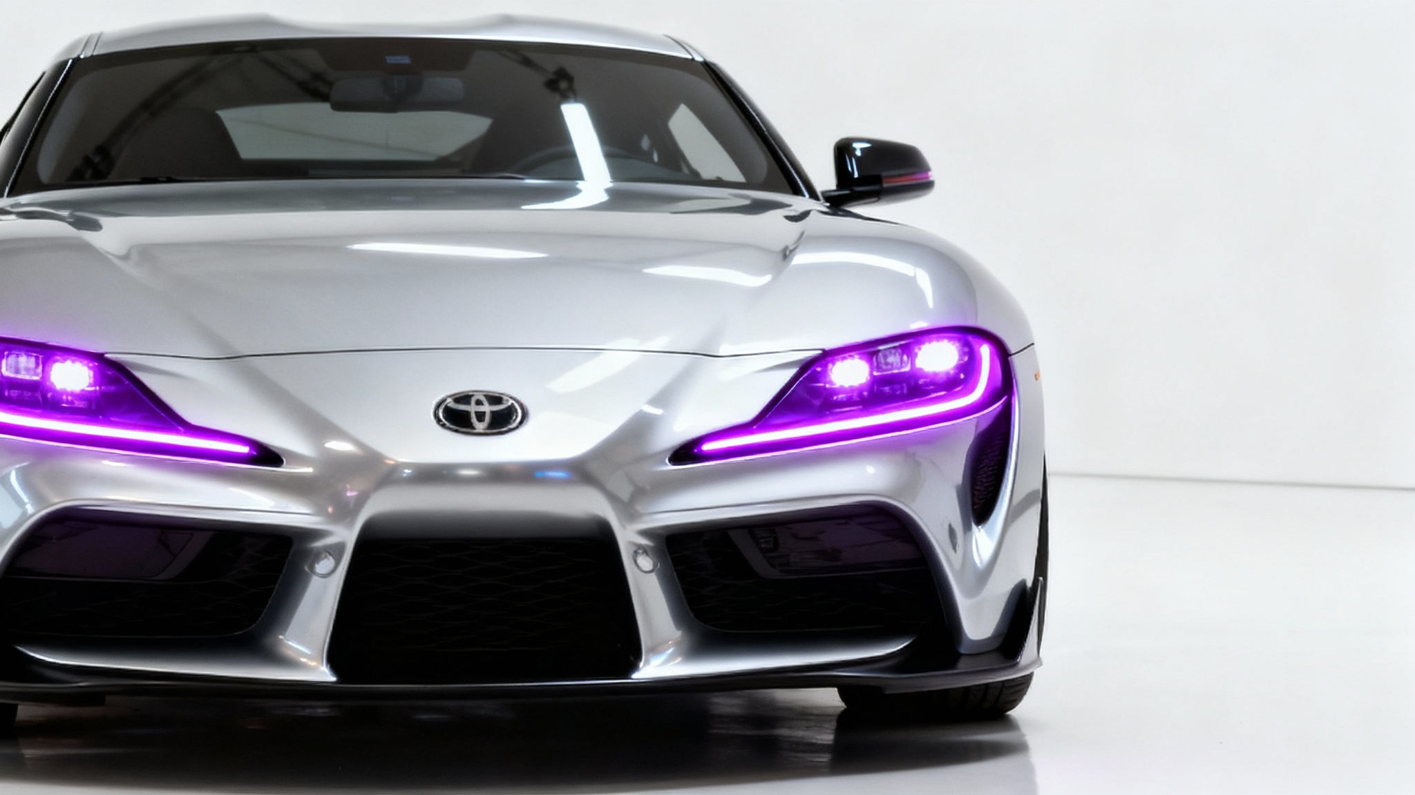 A close-up of a modern silver sports car on a white background, with its headlights shining a bright, custom neon purple.