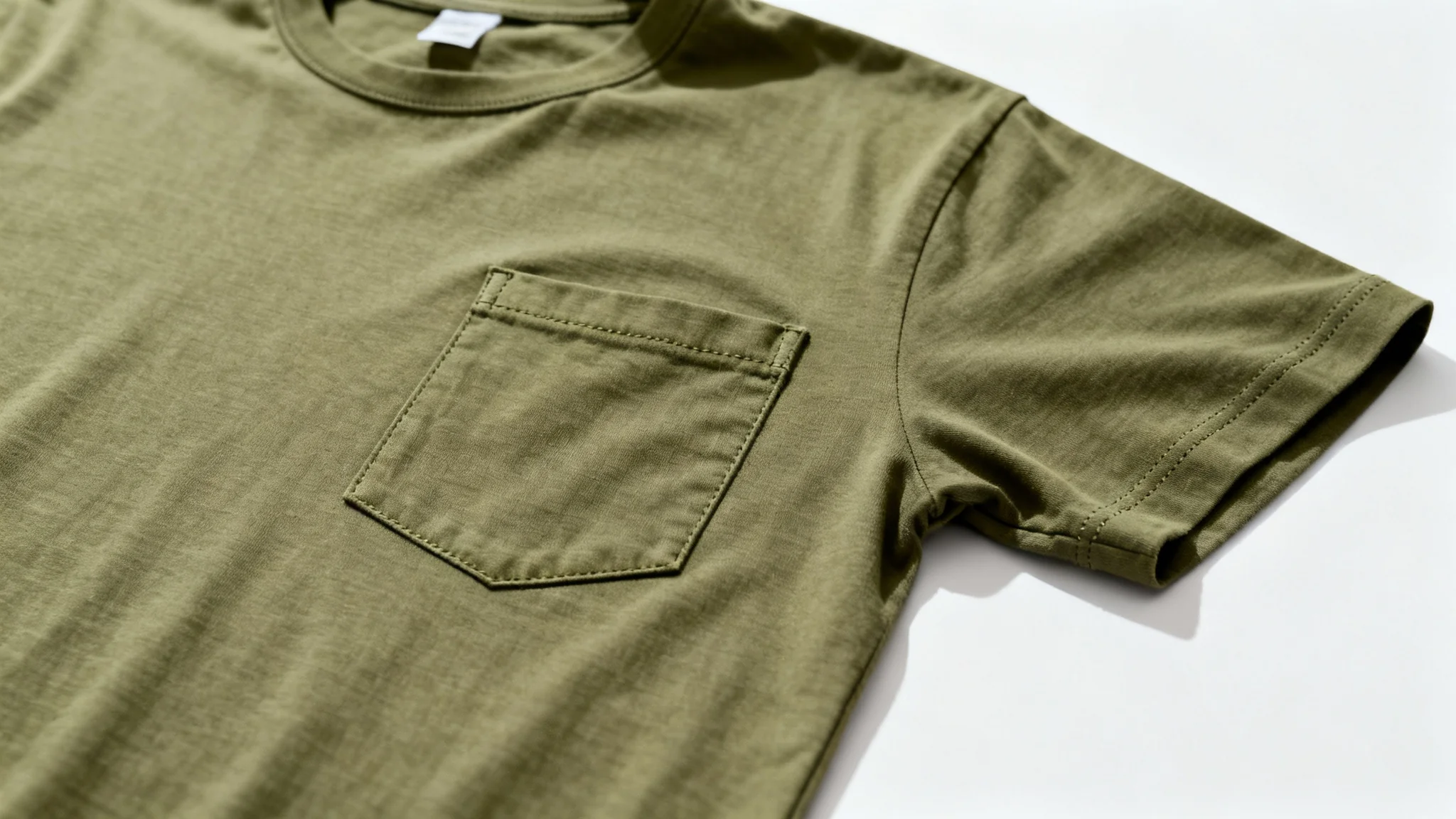 A photorealistic mockup of a muted olive green pocket t-shirt laid flat on a crisp white background, with a close-up on the chest pocket.