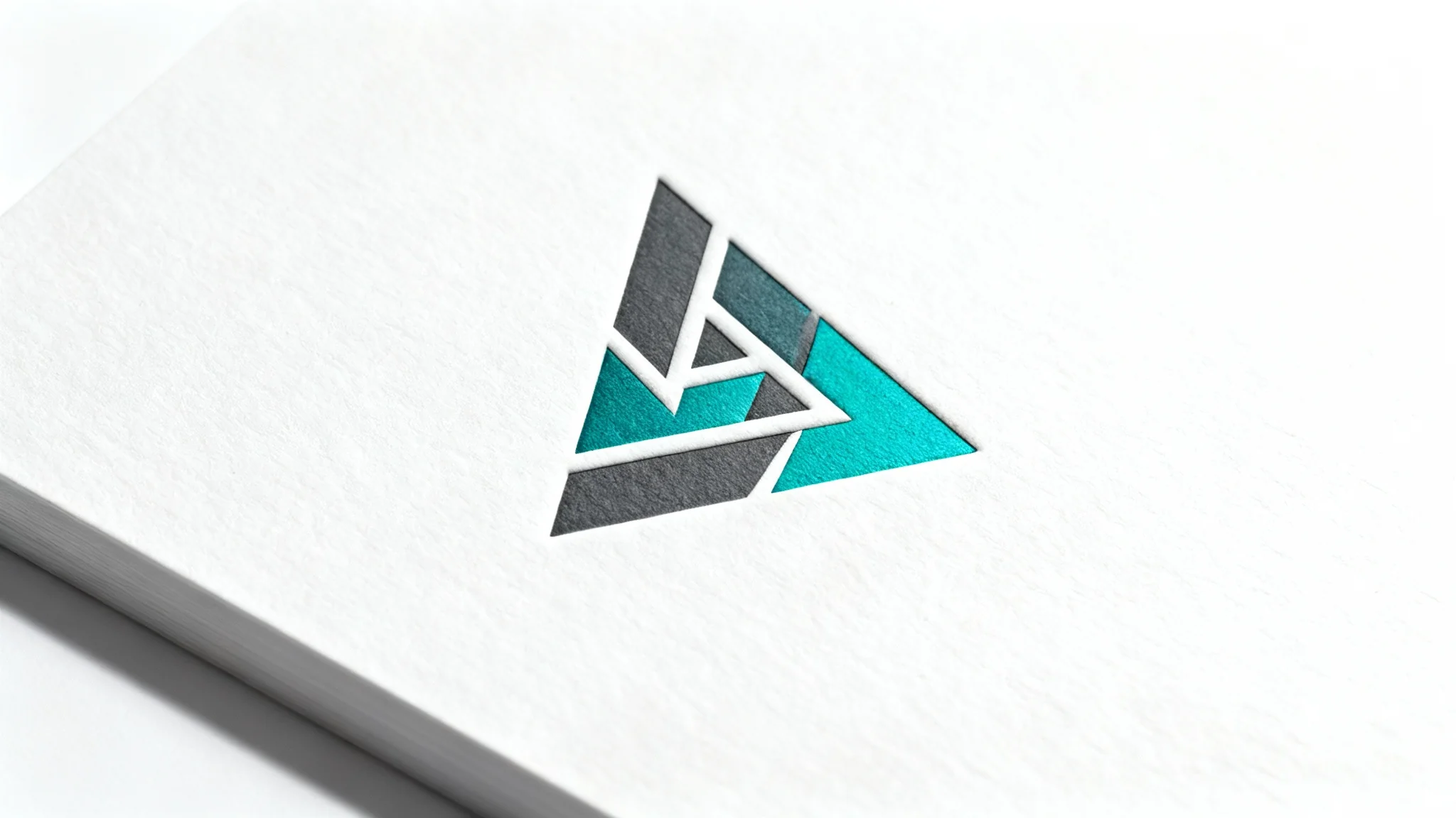 A modern, minimalist triangle logo in charcoal gray and teal, presented as an embossed mockup on white cardstock with a white background.