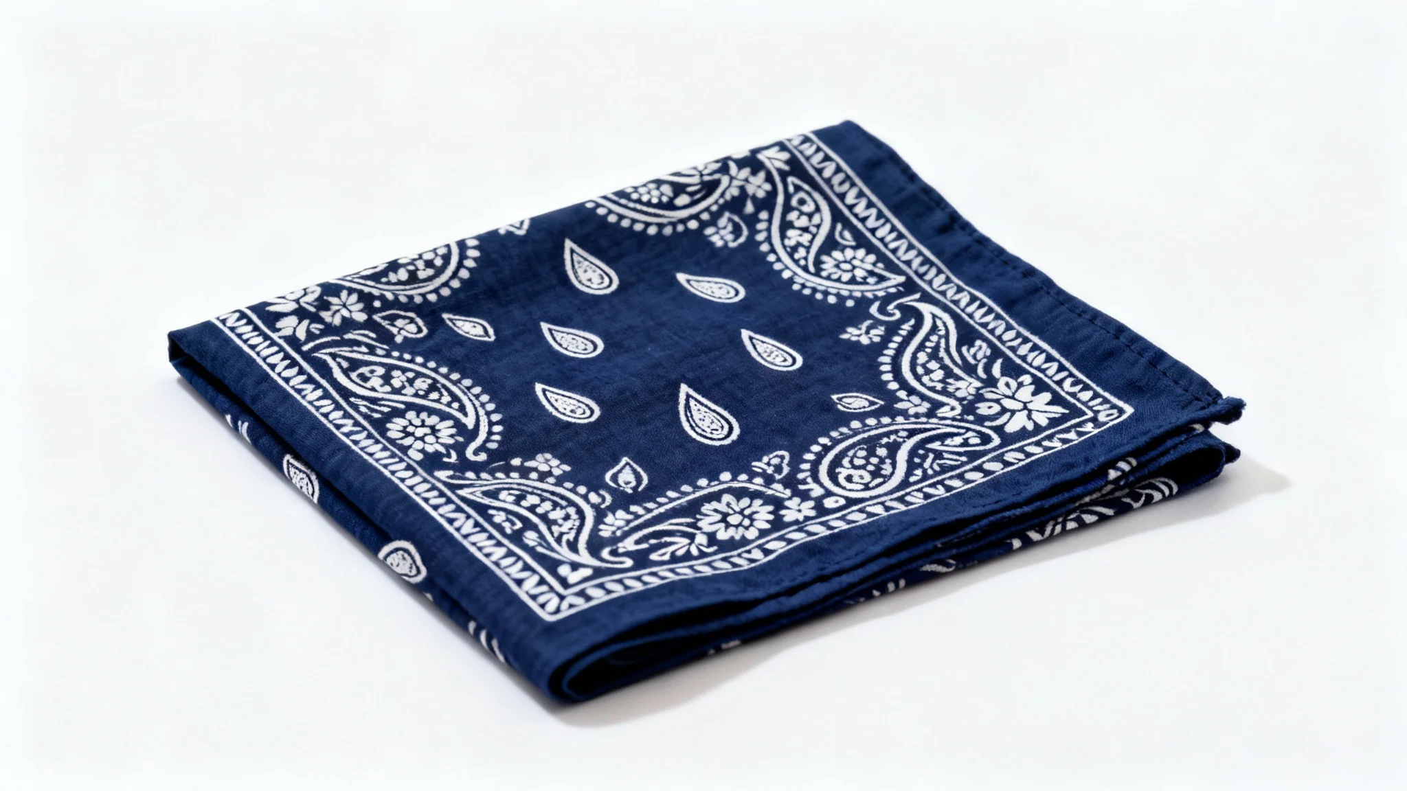 A navy blue bandana with a classic white paisley pattern, neatly folded and displayed on a clean white background.