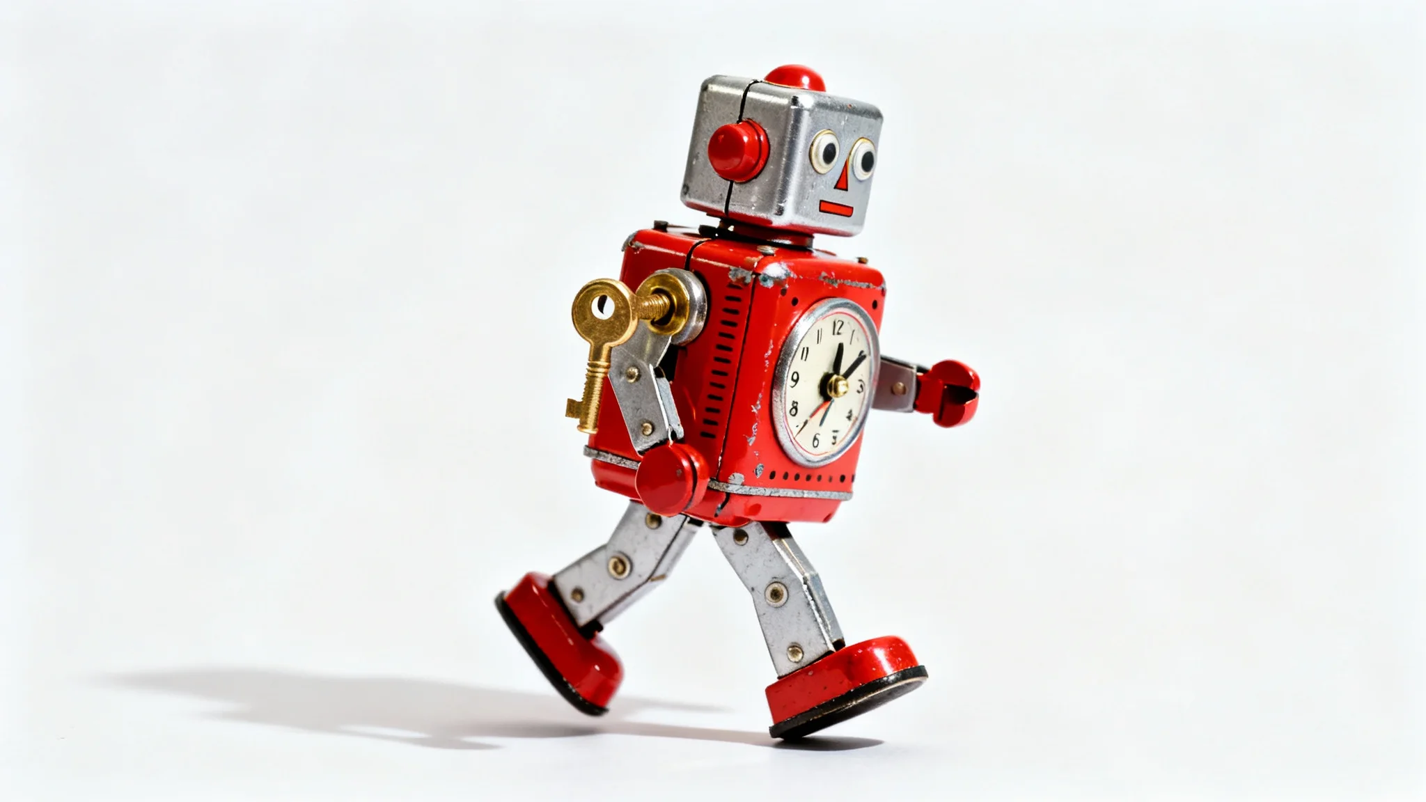 A close-up studio photograph of a vintage-style red and silver clockwork robot toy with a brass key, positioned as if walking against a pure white background.