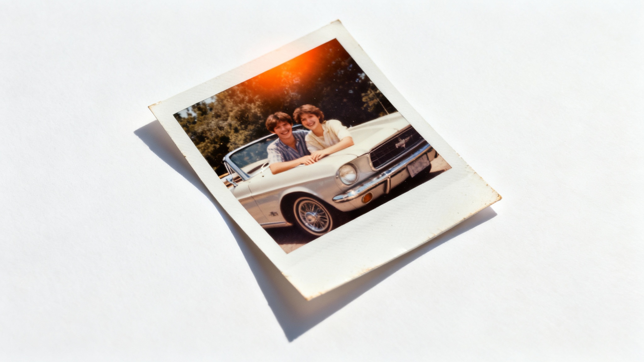 A physical photograph with a vintage effect, showing a couple from the 1980s with a classic car. The photo has faded colors, film grain, and is displayed on a white background.