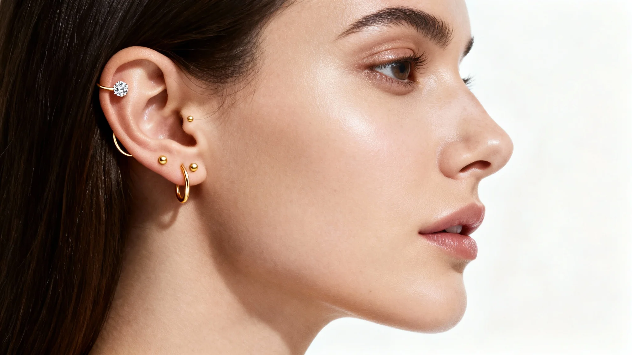 A hyper-realistic close-up of a person's ear featuring several delicate gold and diamond piercings, set against a clean white background to showcase a virtual piercing try-on.