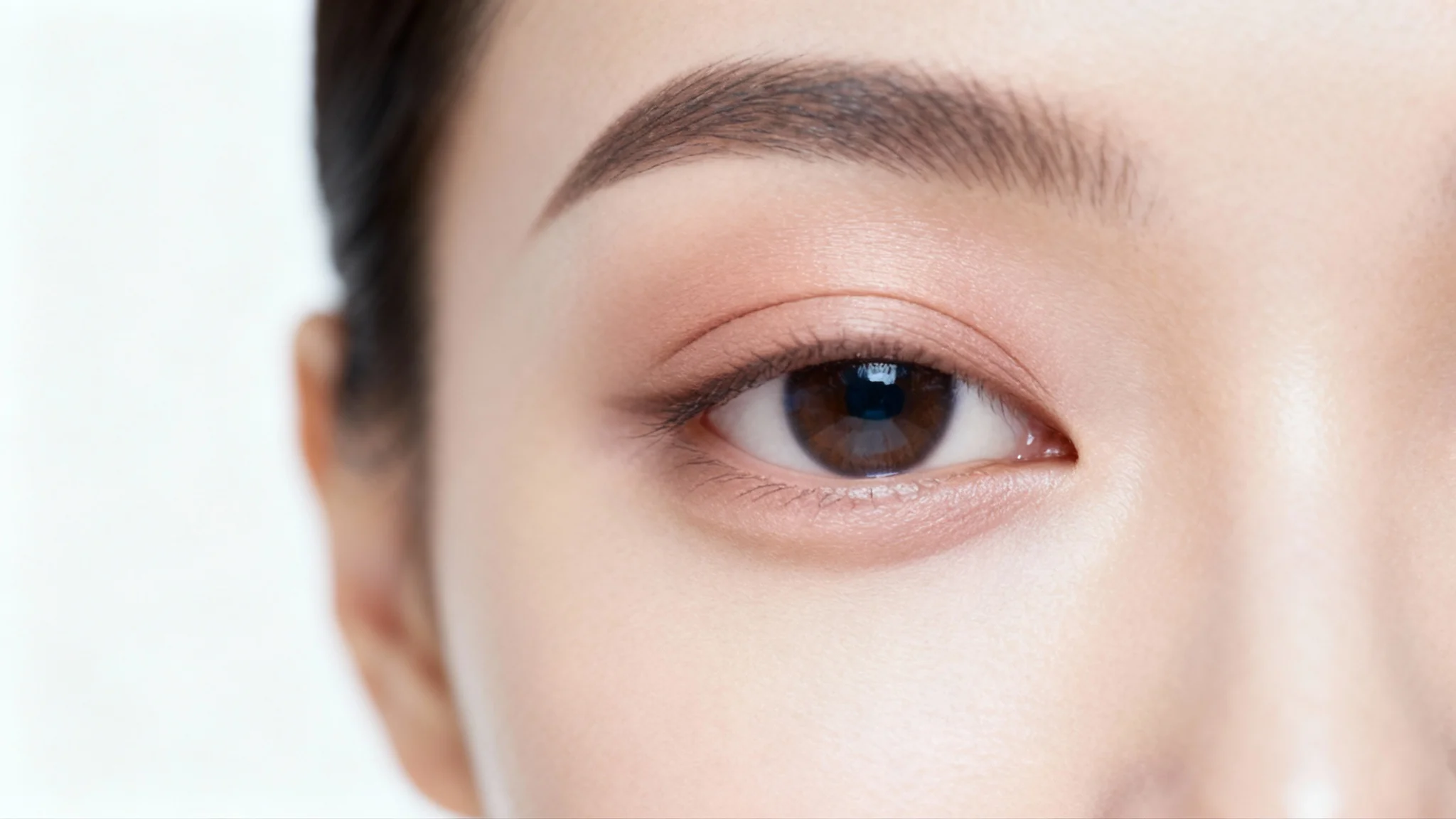A hyper-realistic macro photograph of a woman's eye, showcasing flawless skin and a clean eyelid with no eyelashes, representing a photo editing effect, against a plain white background.