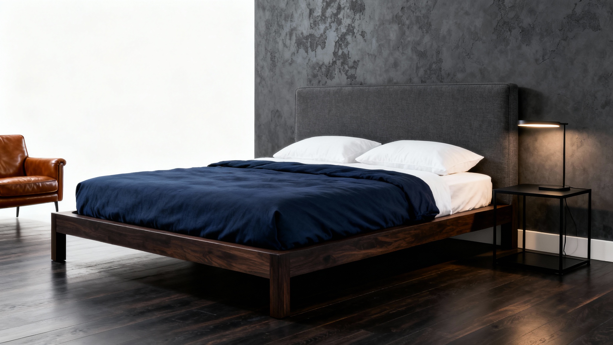 A sophisticated masculine bedroom design featuring a dark wood bed with a navy duvet, a cognac leather armchair, and a dark accent wall, all displayed against a clean white background.