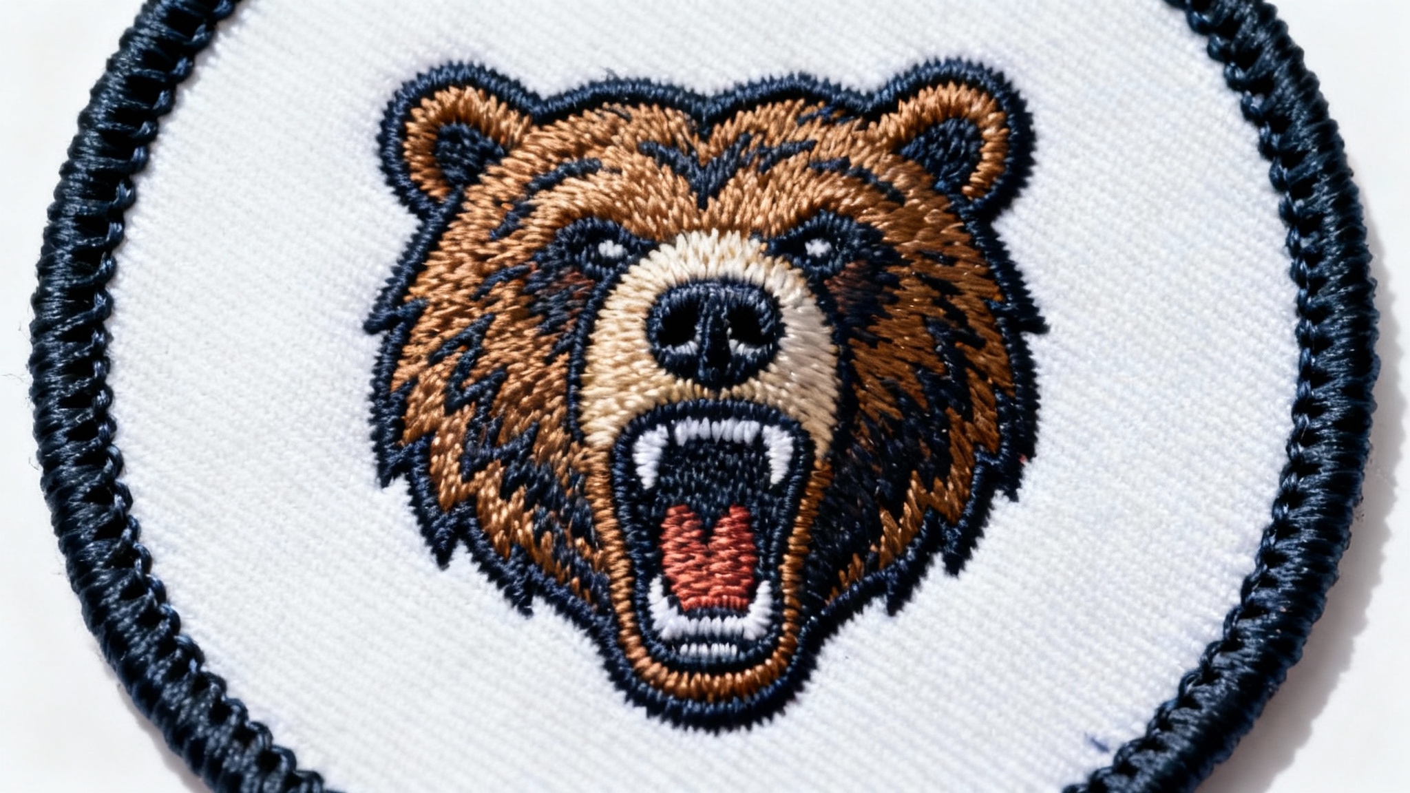A detailed, photorealistic close-up of a circular embroidered patch with a roaring bear design, highlighting its thick and professionally stitched merrowed edge, on a clean white background.