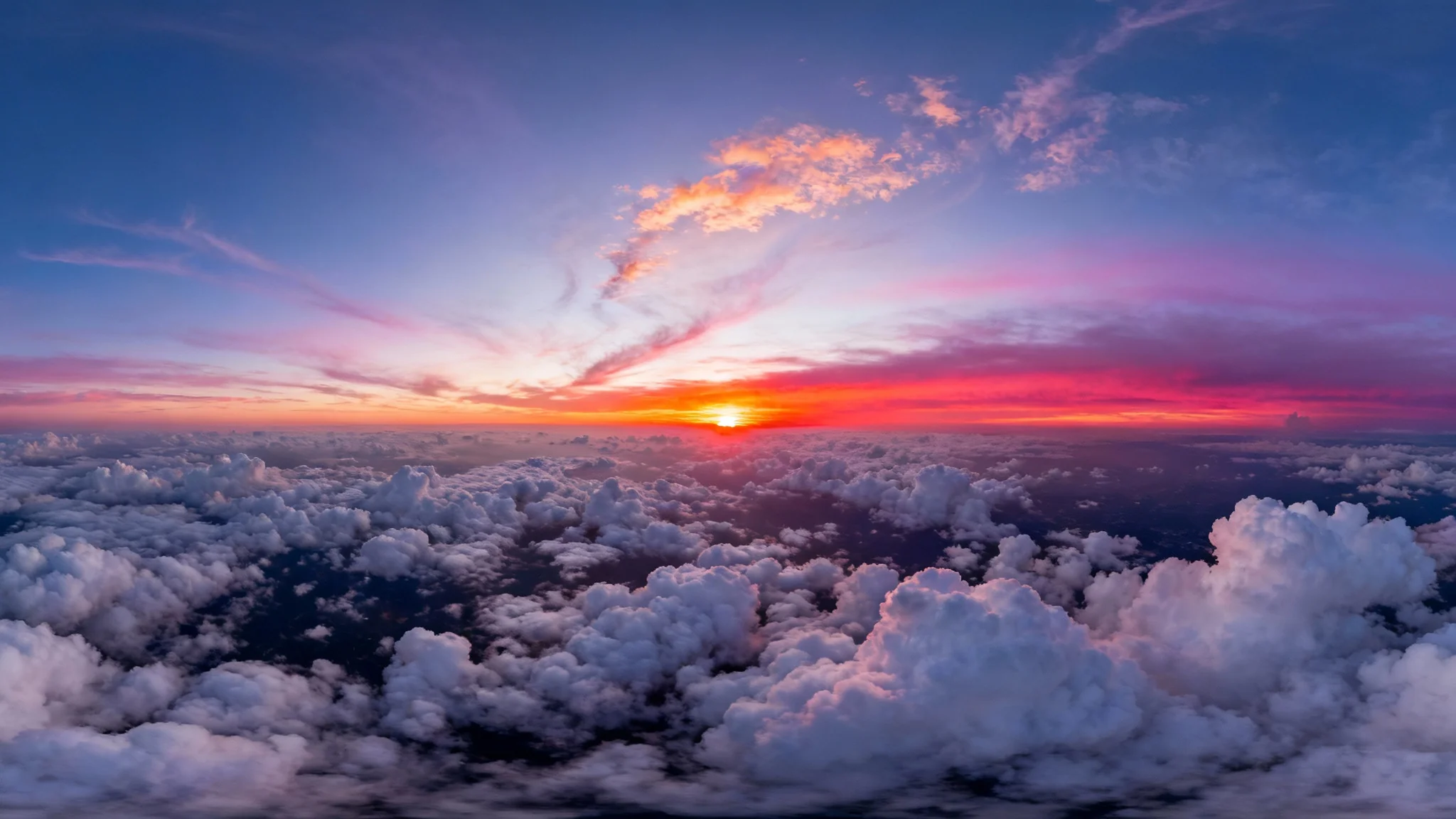 A stunning 360-degree panoramic image of a vibrant sunset sky viewed from above a sea of clouds, with the sky painted in brilliant shades of orange, pink, and purple.