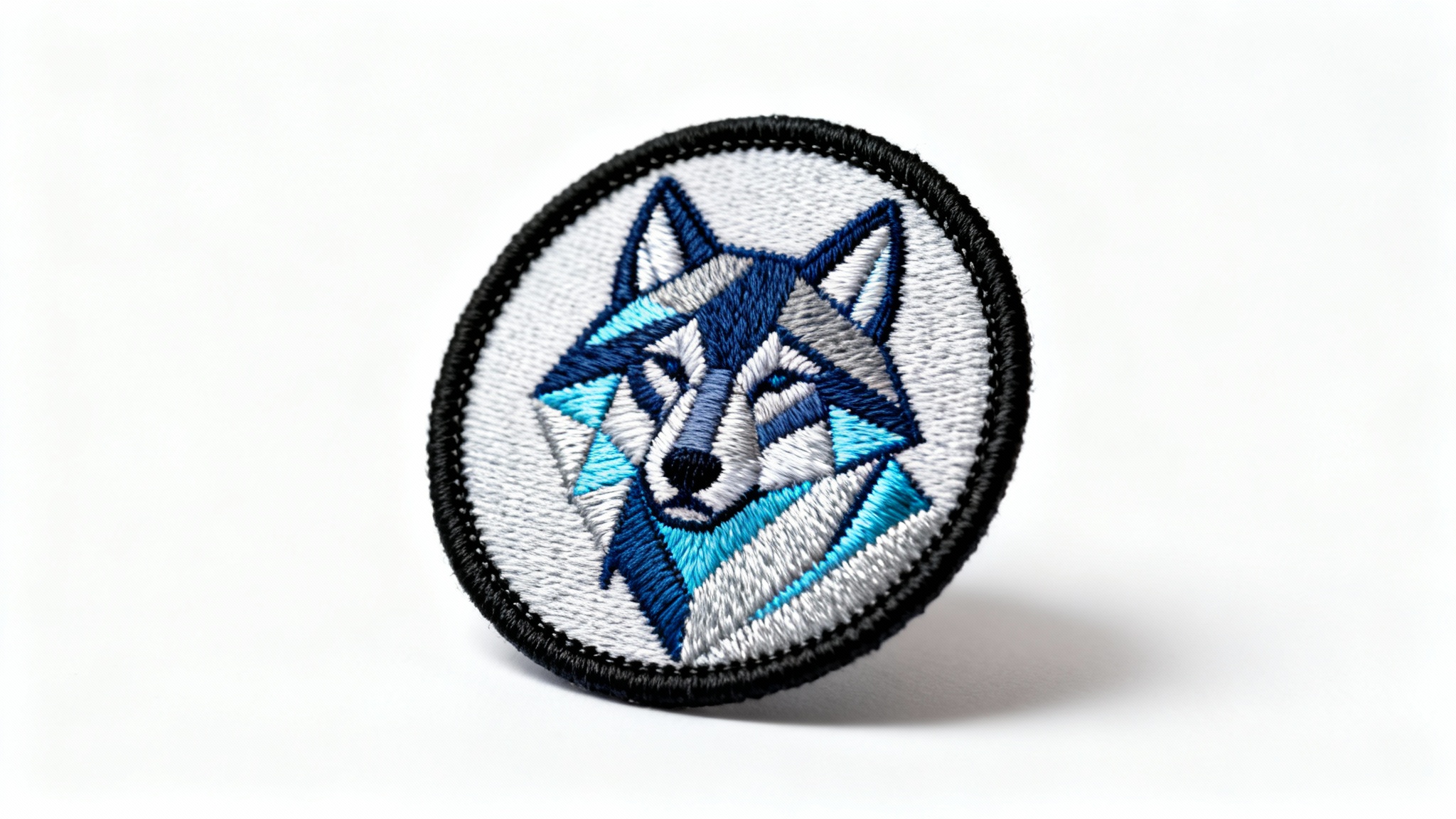 A detailed, circular embroidered patch featuring a geometric wolf head design in shades of blue and gray, displayed on a clean white background.