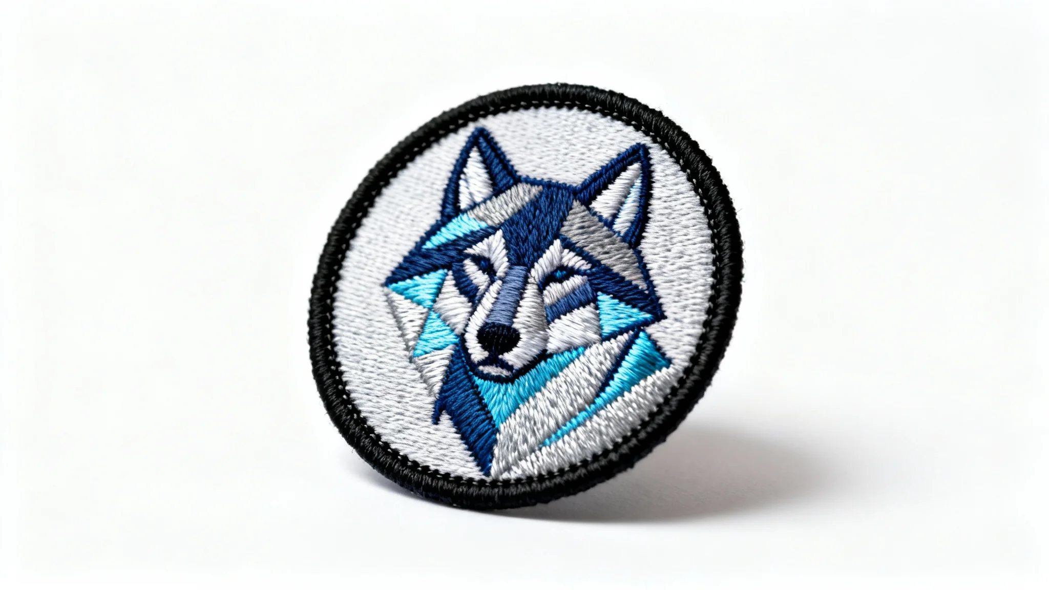 A detailed, circular embroidered patch featuring a geometric wolf head design in shades of blue and gray, displayed on a clean white background.