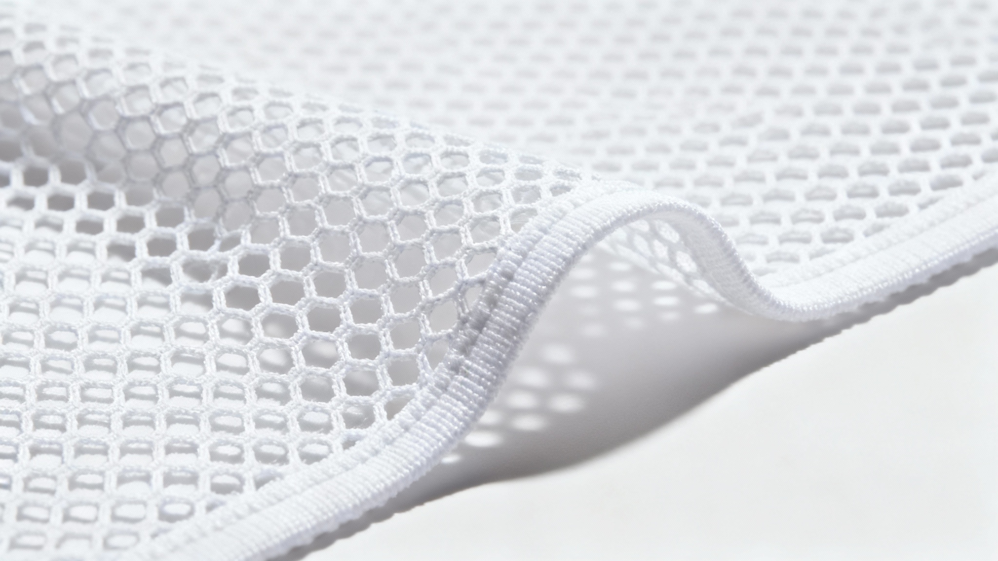 A detailed macro shot of a clean, white mesh fabric, highlighting the hexagonal weave and texture against a solid white background.