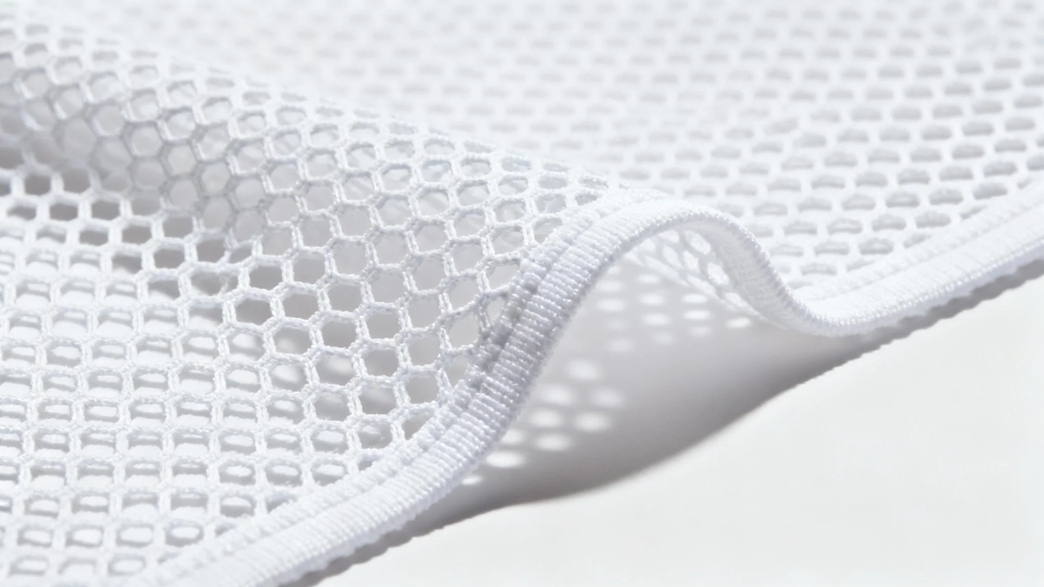 A detailed macro shot of a clean, white mesh fabric, highlighting the hexagonal weave and texture against a solid white background.