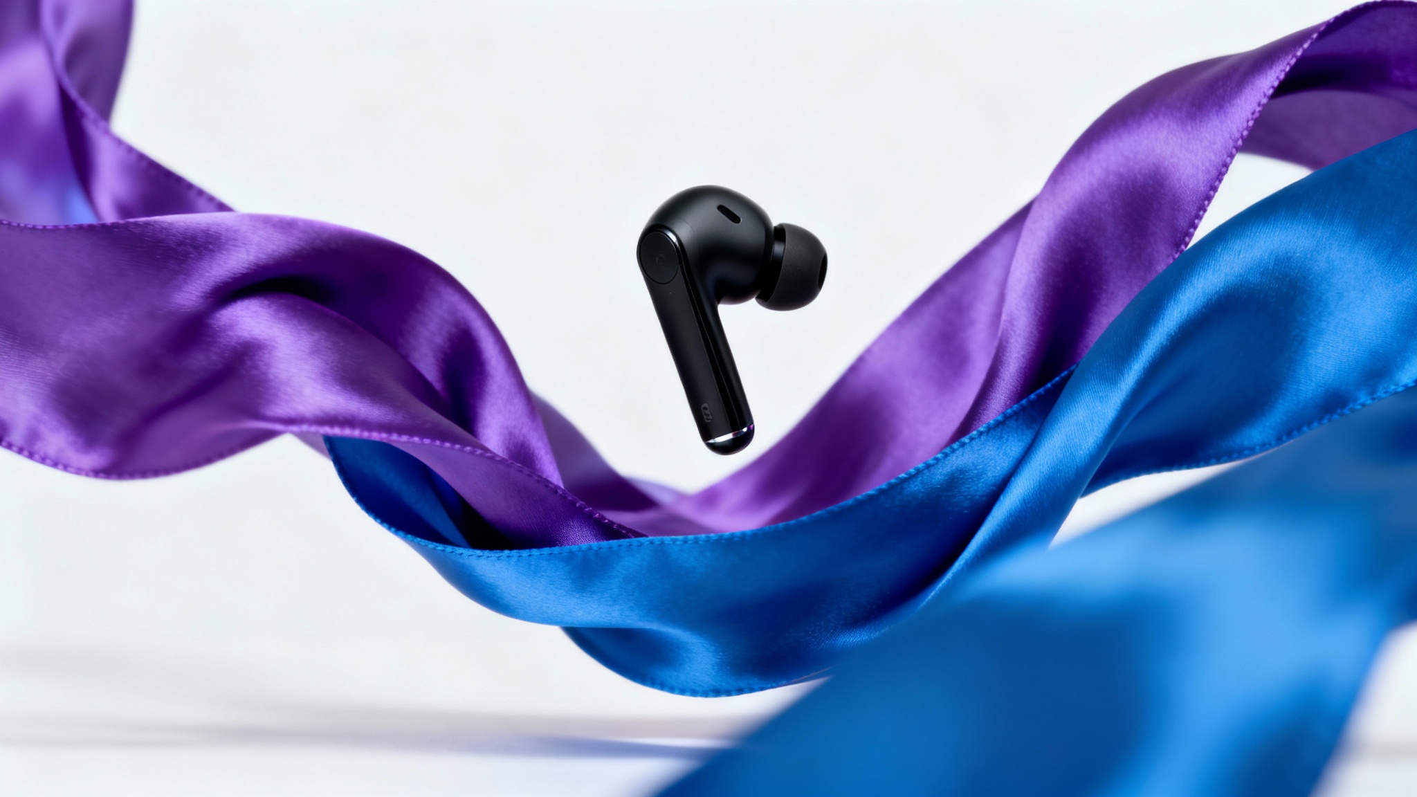 A photorealistic image of a sleek black wireless earbud levitating against a white background, with a swirl of purple and blue silk fabric dramatically unveiling it.