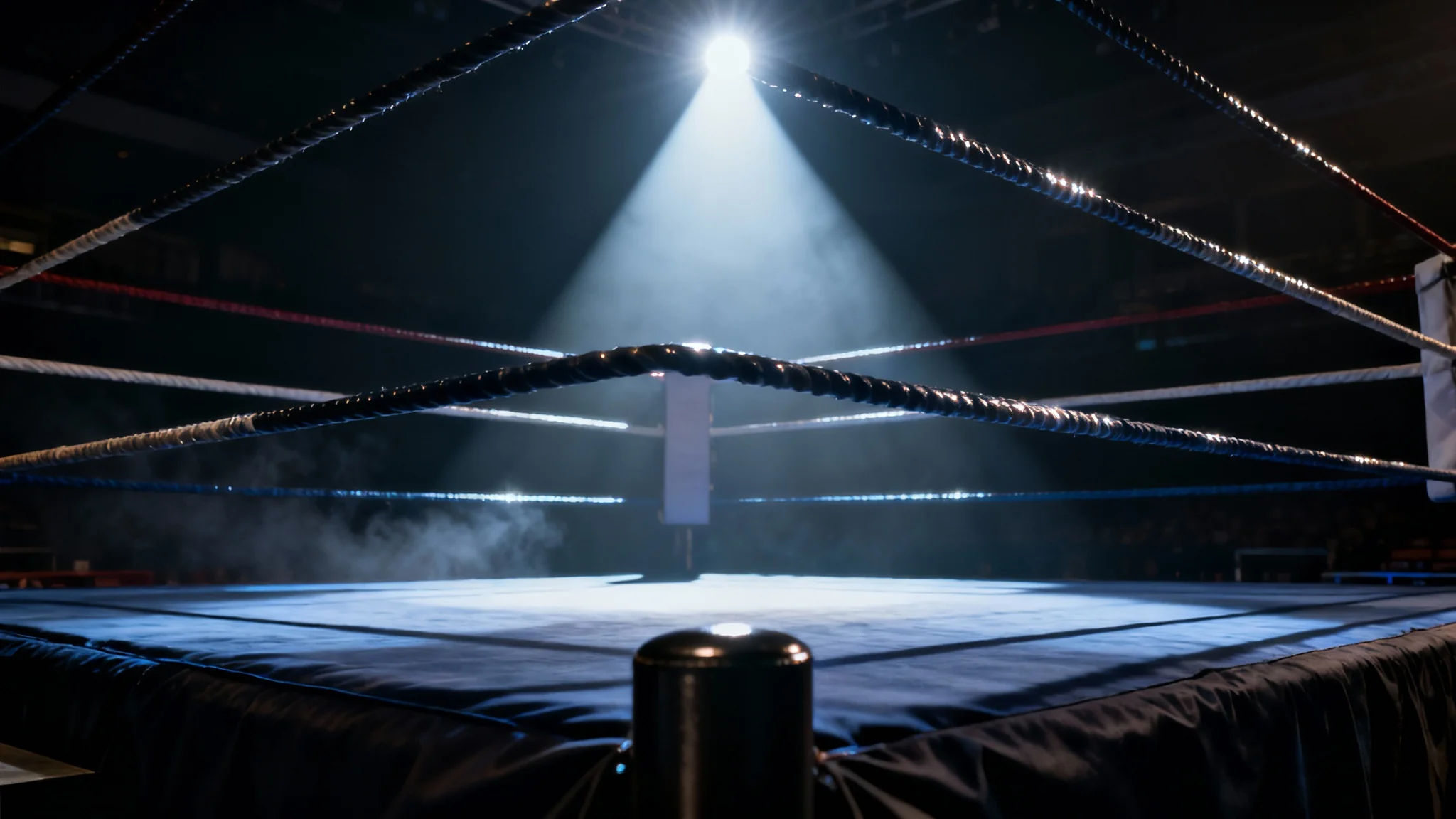 A dramatic, low-angle shot of an empty boxing ring under a single spotlight, with a dark, hazy arena in the background, creating a sense of anticipation.