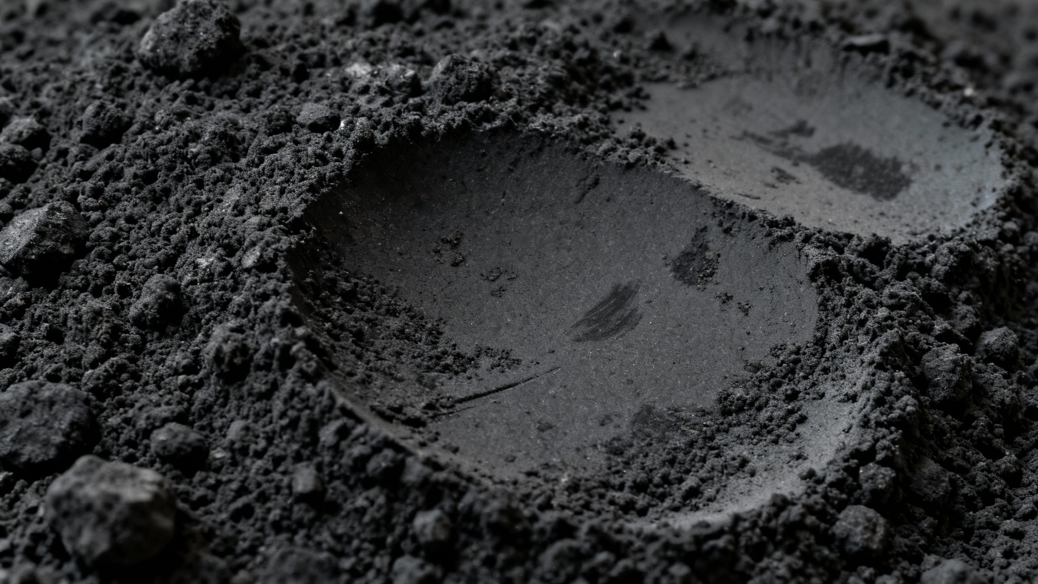 A close-up, high-resolution image of a black charcoal texture, showing its rough, gritty surface and varying shades of dark gray.