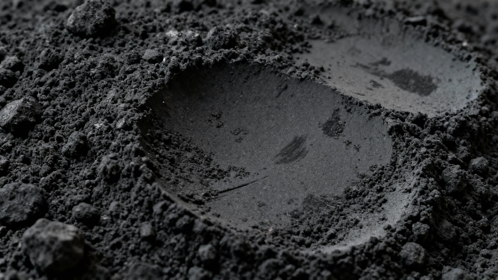 A close-up, high-resolution image of a black charcoal texture, showing its rough, gritty surface and varying shades of dark gray.