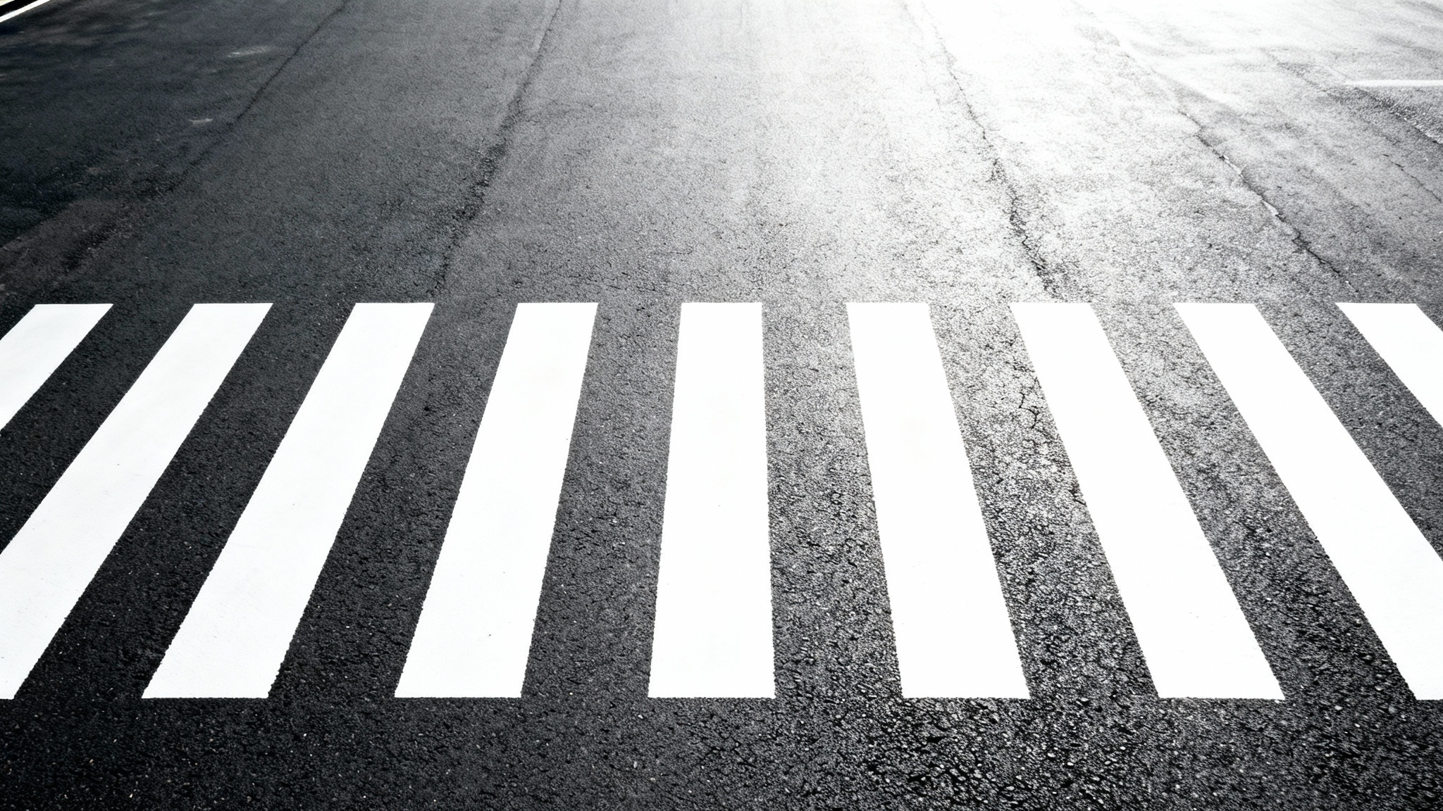 A minimalist, top-down aerial view of a white zebra crosswalk on a dark asphalt road, isolated against a plain white background.