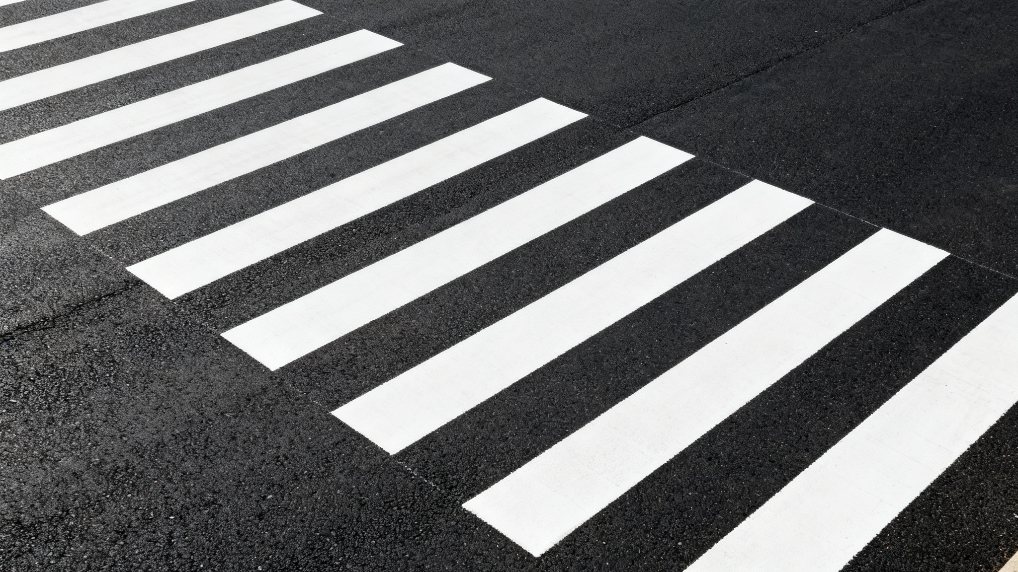 A clean, minimalist top-down photograph of an empty crosswalk with bold white stripes on a dark, uniform asphalt road.