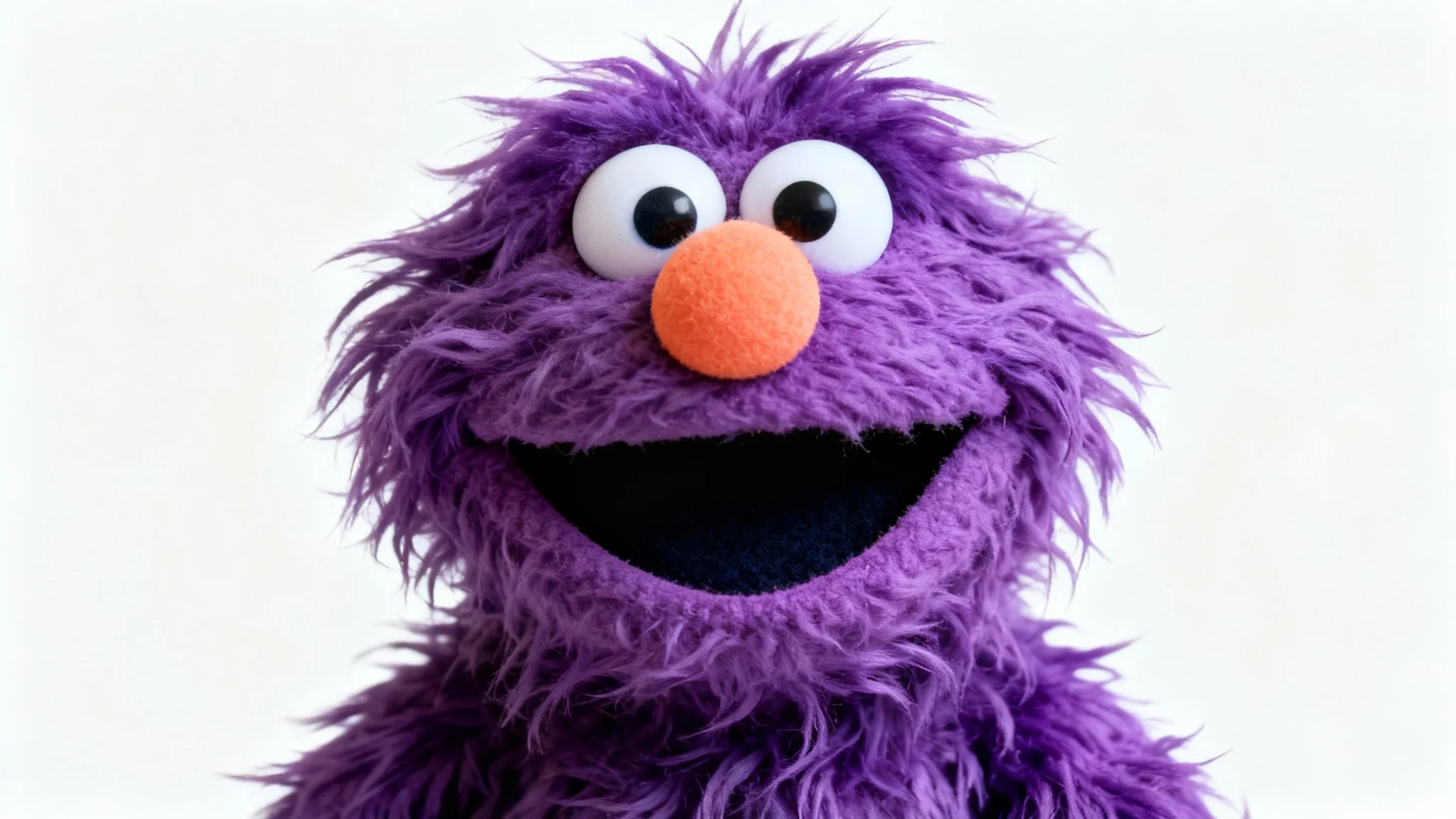 A high-quality studio photograph of a friendly muppet puppet with shaggy purple fur, big googly eyes, and an orange nose, smiling against a plain white background.