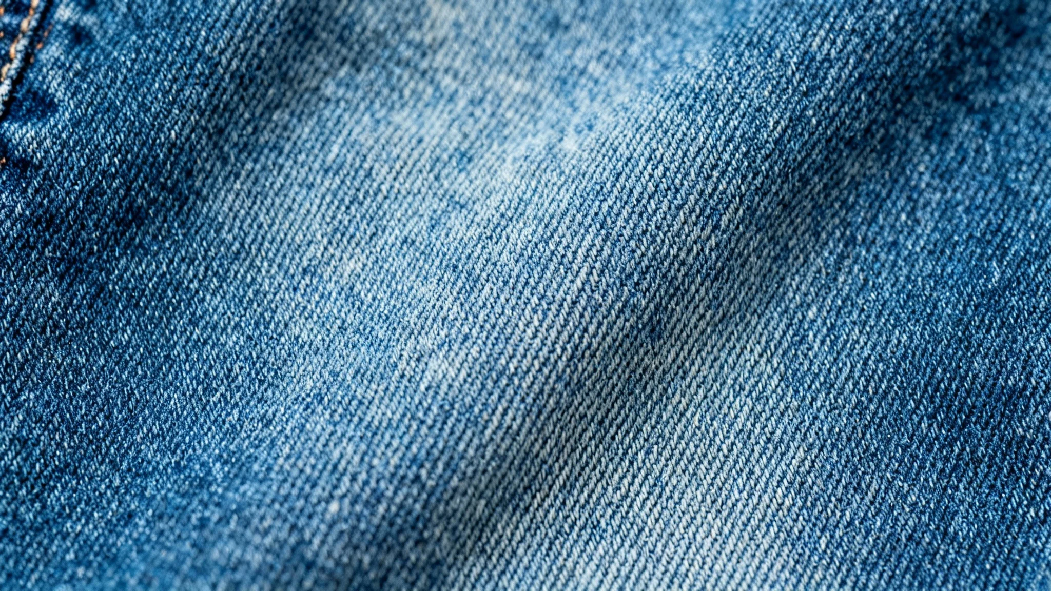 A detailed, high-resolution macro shot of a blue denim jeans texture, showing the diagonal weave and individual cotton fibers clearly.