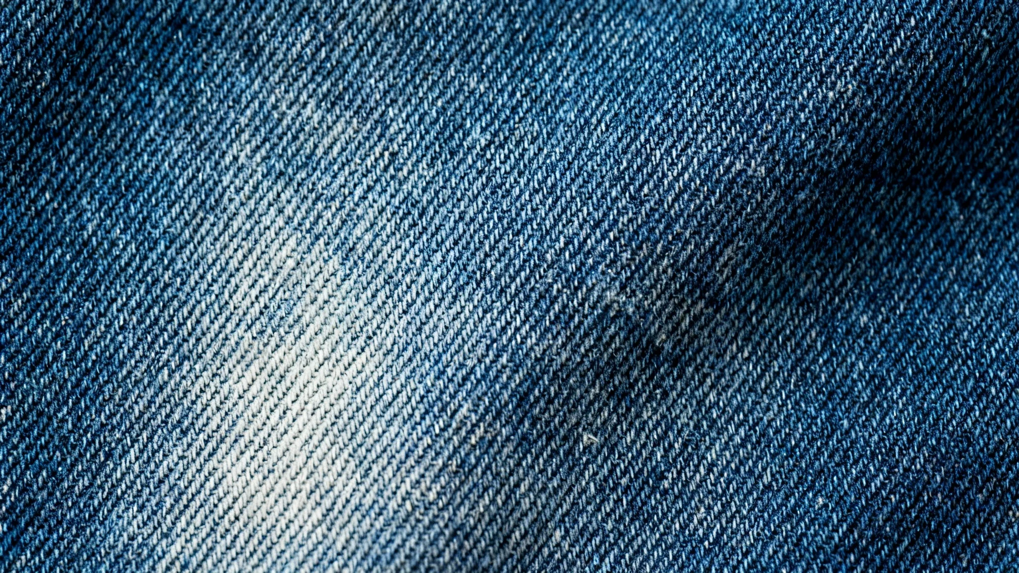 A close-up macro shot of a blue denim jeans texture, showing the detailed twill weave and fabric fibers.