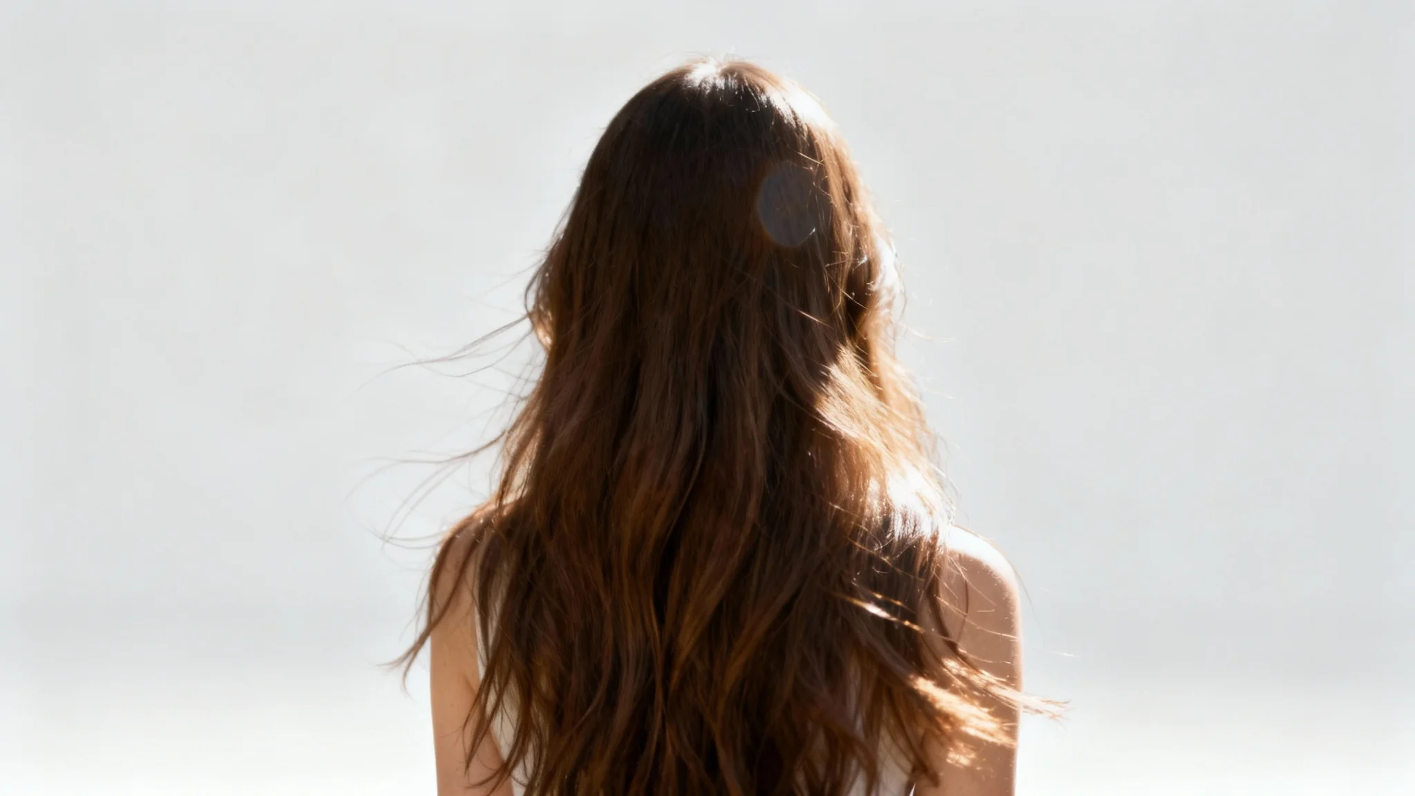 A demonstration of a perfect hair masking result, showing a woman with long, flowing brown hair perfectly isolated from her original background and placed onto a clean, light gray backdrop. The detail in every hair strand is visible.