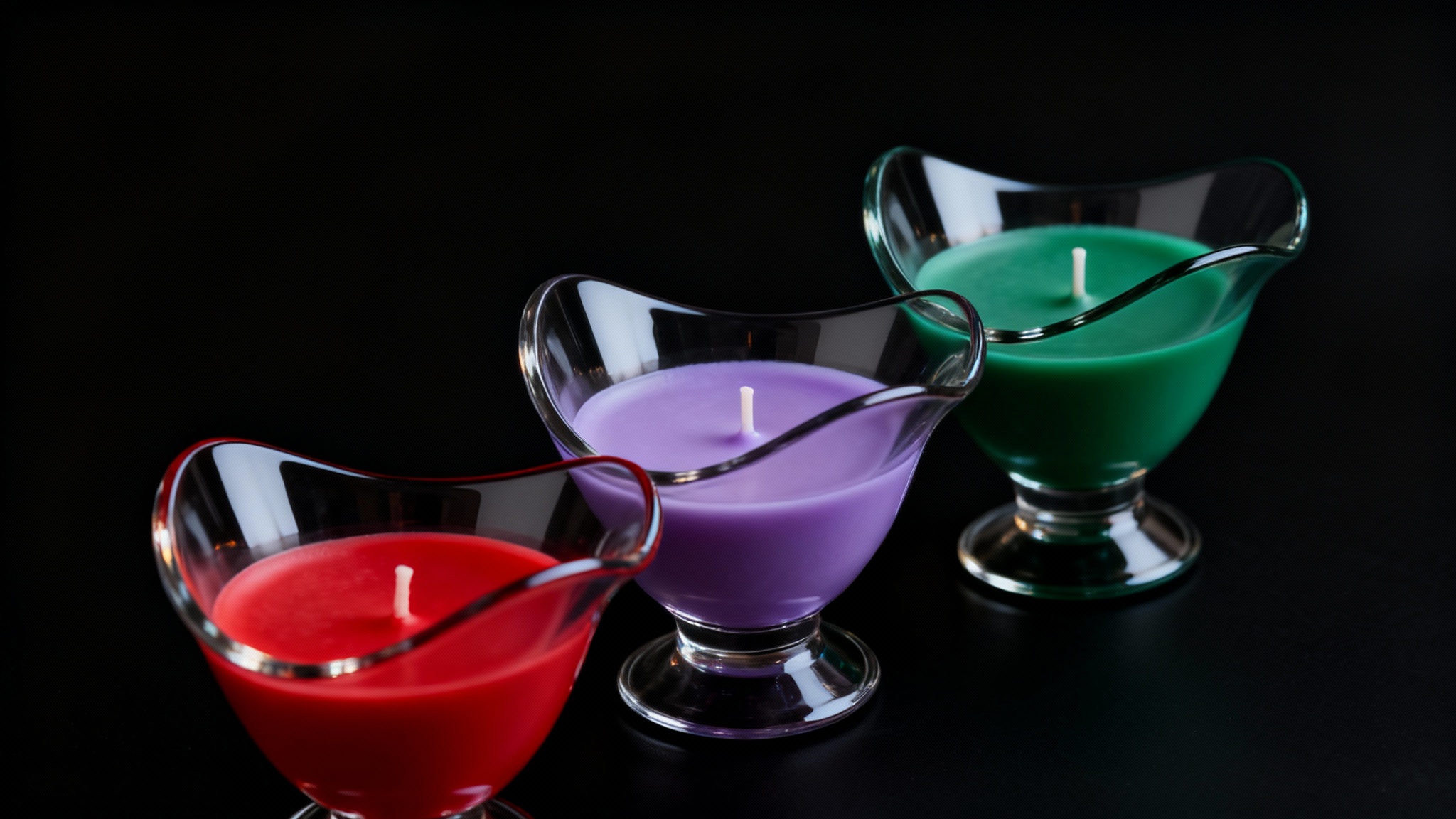 A professional studio photograph of three elegant glass candle holders with colorful wax, dramatically lit against a stark black background, creating a luxurious and modern feel.