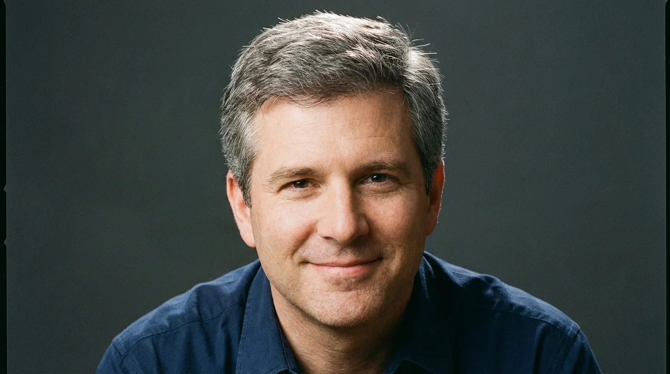 Close-up portrait of a smiling man in his late 40s with a full head of short salt-and-pepper hair against a dark gray background.