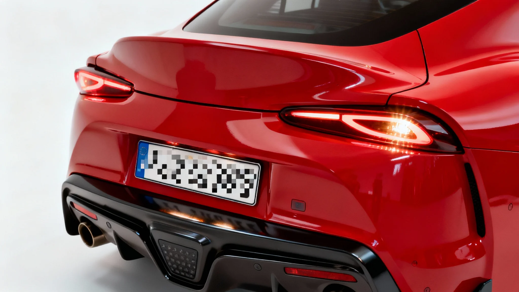 A close-up of the back of a red car with the license plate completely blurred out, shown against a plain white background.