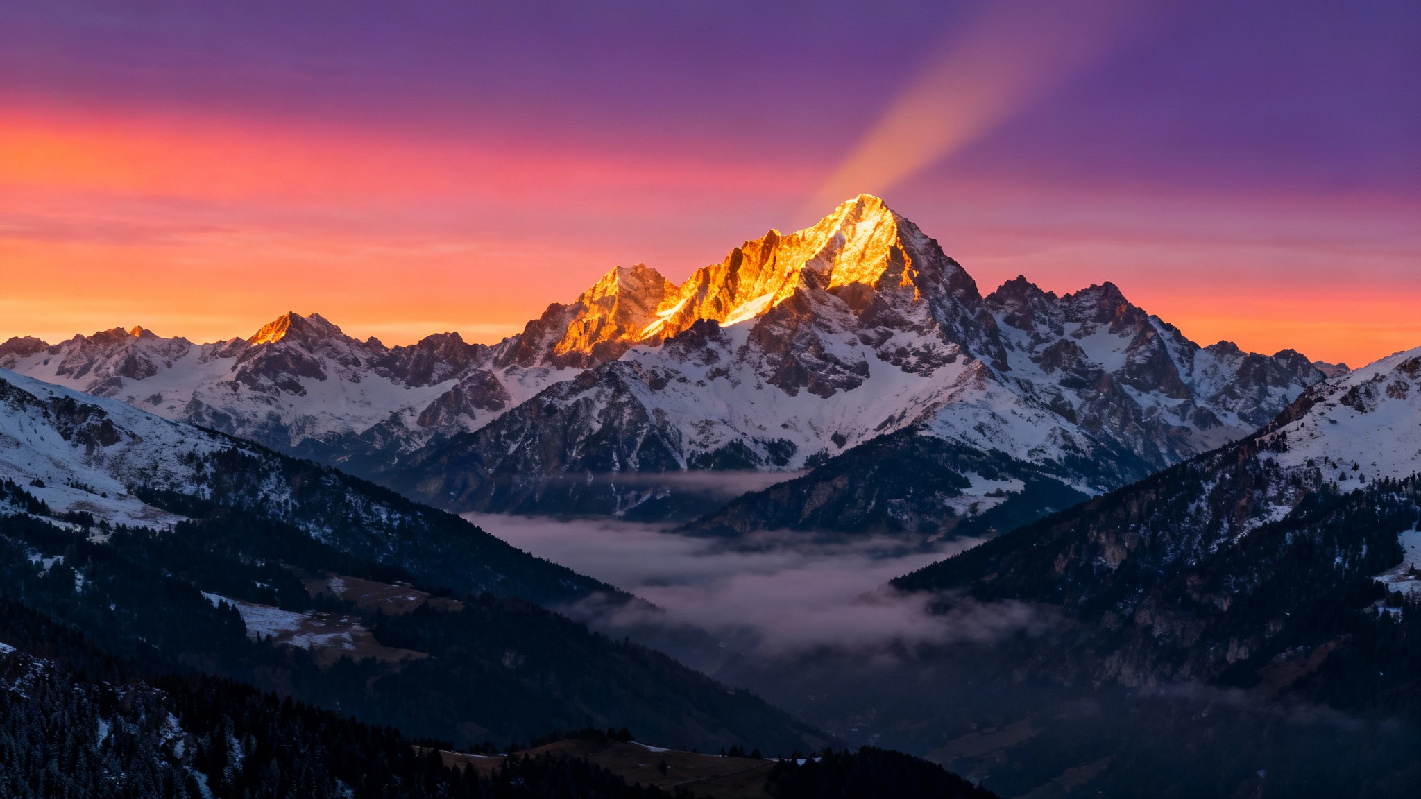 A majestic ultrawide wallpaper of a snow-capped mountain range at sunrise, with vibrant colors in the sky and mist in the valleys.