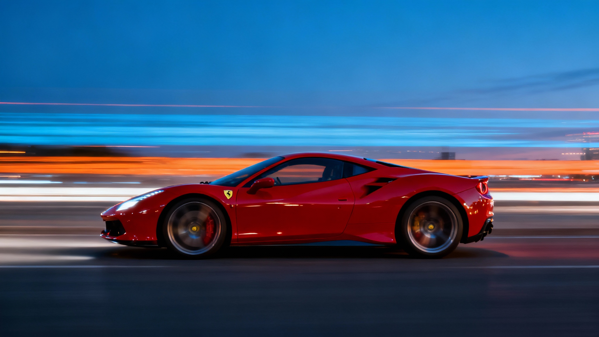 A photorealistic image of a red sports car captured with a panning motion blur effect. The car is in sharp focus, while the city light background is blurred into horizontal streaks, demonstrating speed.
