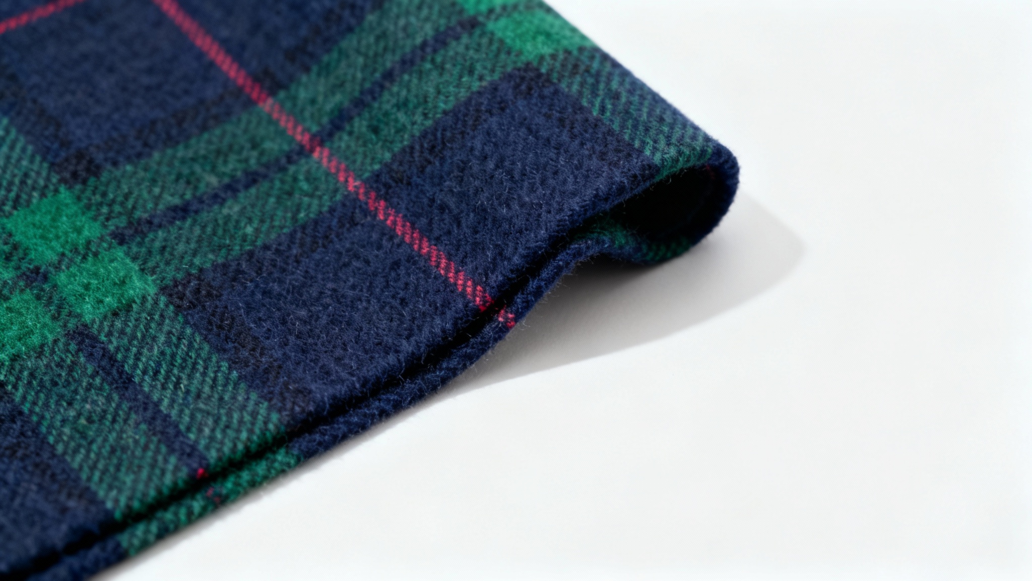 A photorealistic mockup of a folded piece of classic tartan plaid fabric in navy blue and forest green, displayed against a solid white background.