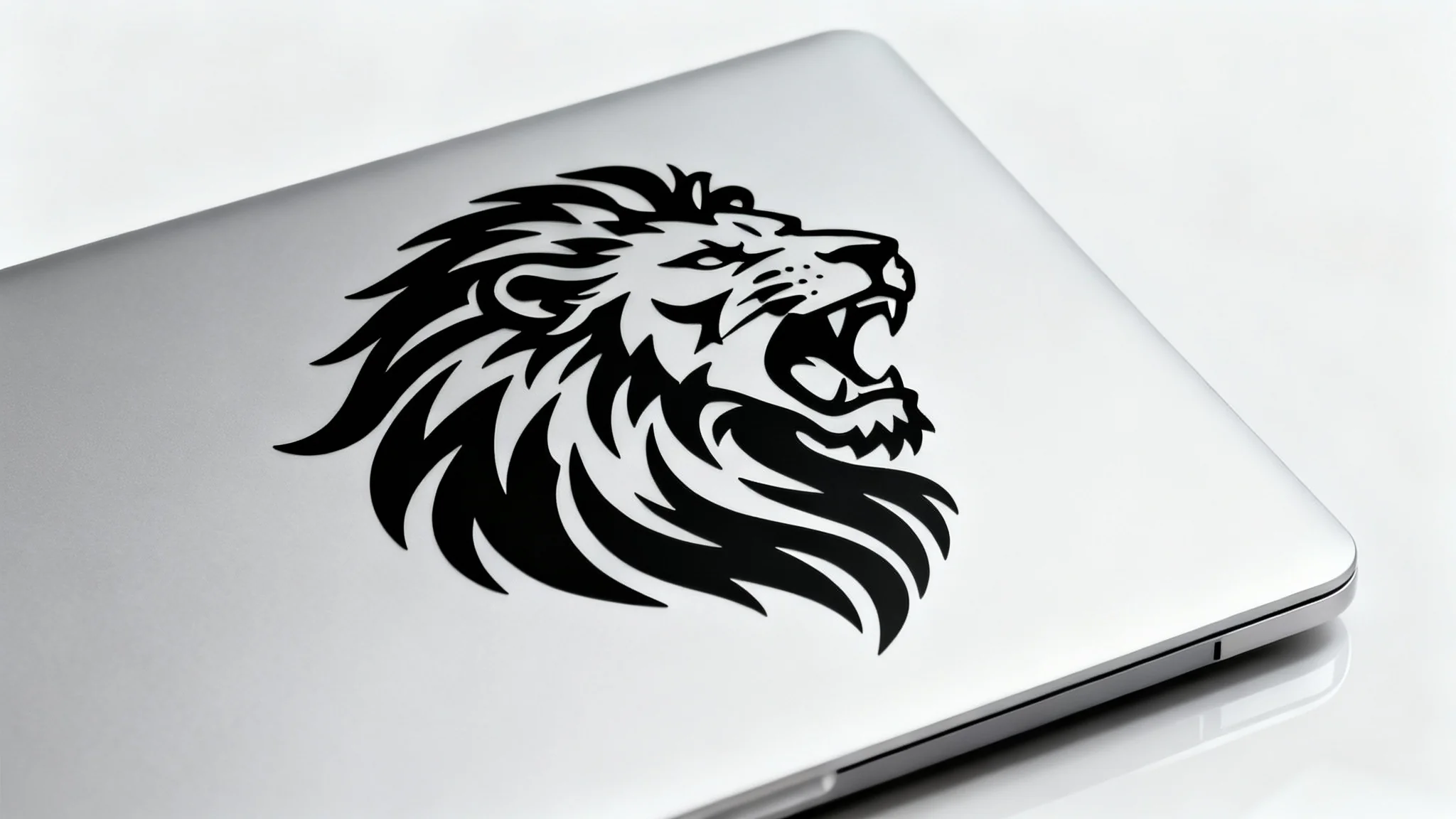 A close-up product photo of a matte black vinyl decal of a roaring lion's head applied to the corner of a silver laptop, set against a clean white background.