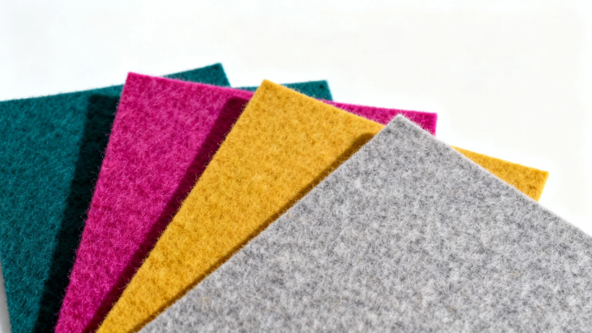 A vibrant collection of felt texture sheets in teal, fuchsia, yellow, and gray, fanned out on a white background to showcase their soft, fibrous material.
